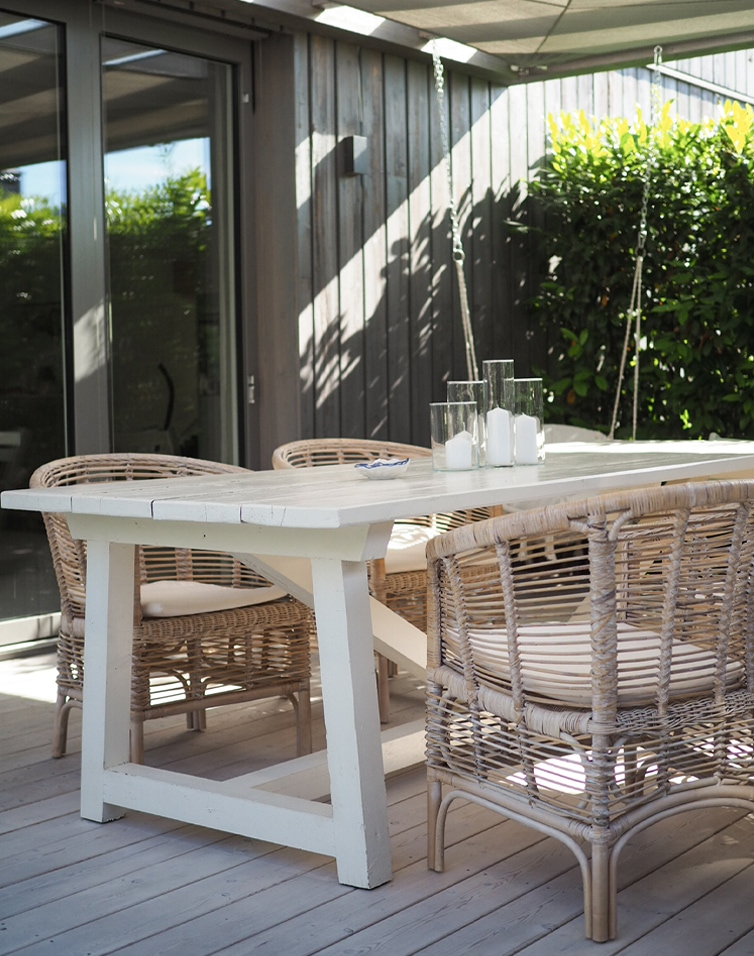 Tavolo da giardino in legno bianco con sedie in vimini naturale e candele in contenitori di vetro