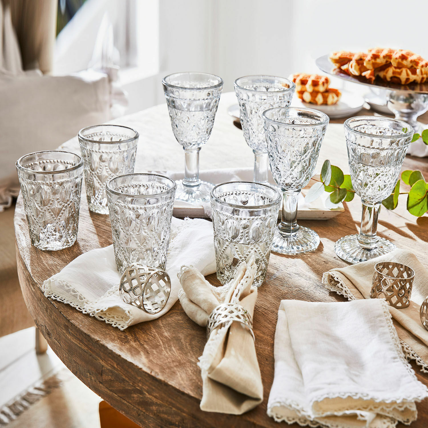 Set di 8 bicchieri Vérane Set di bicchieri e calici in vetro trasparente con motivo decorativo su tavolo in legno con tovaglioli