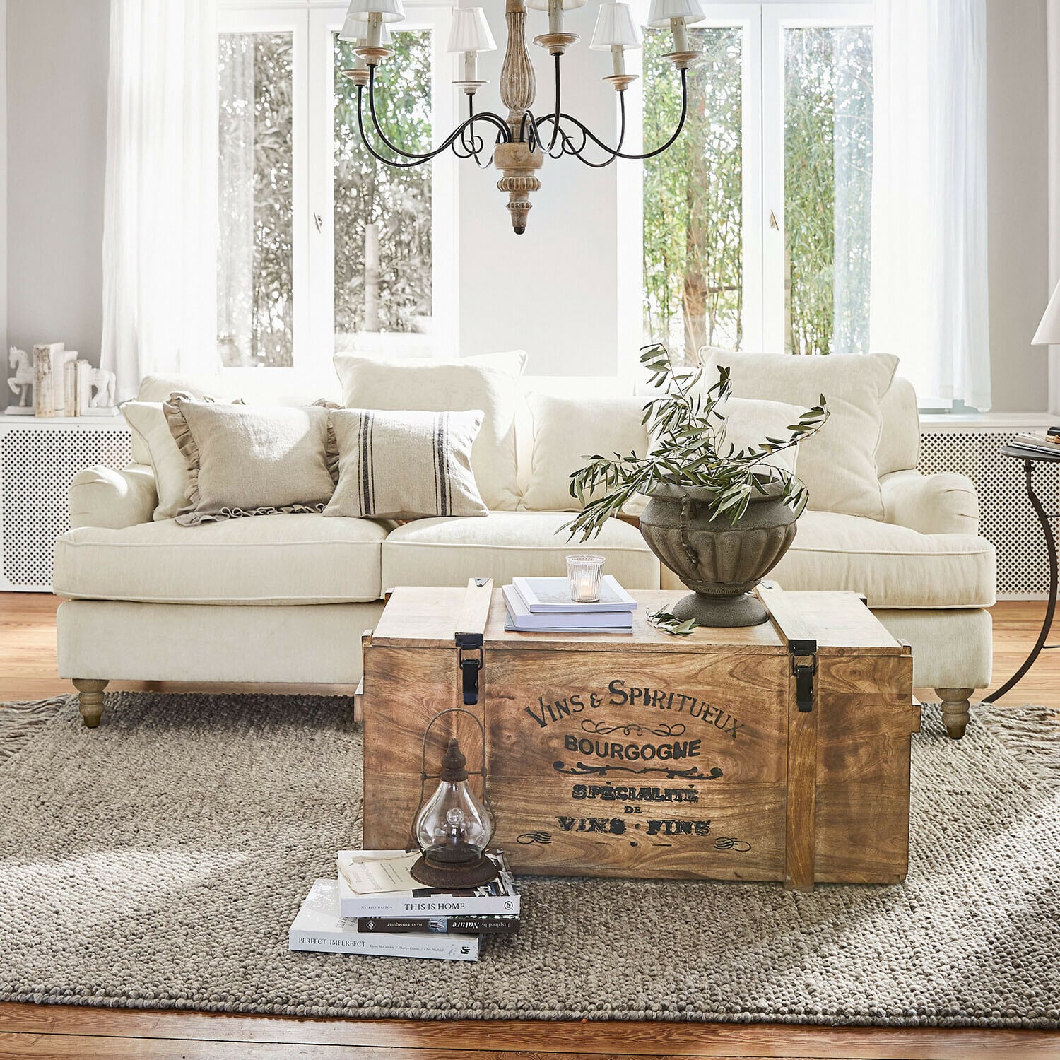 Divano Isa Baule in legno con scritta vintage usato come tavolino in soggiorno luminoso con divano beige e decorazioni
