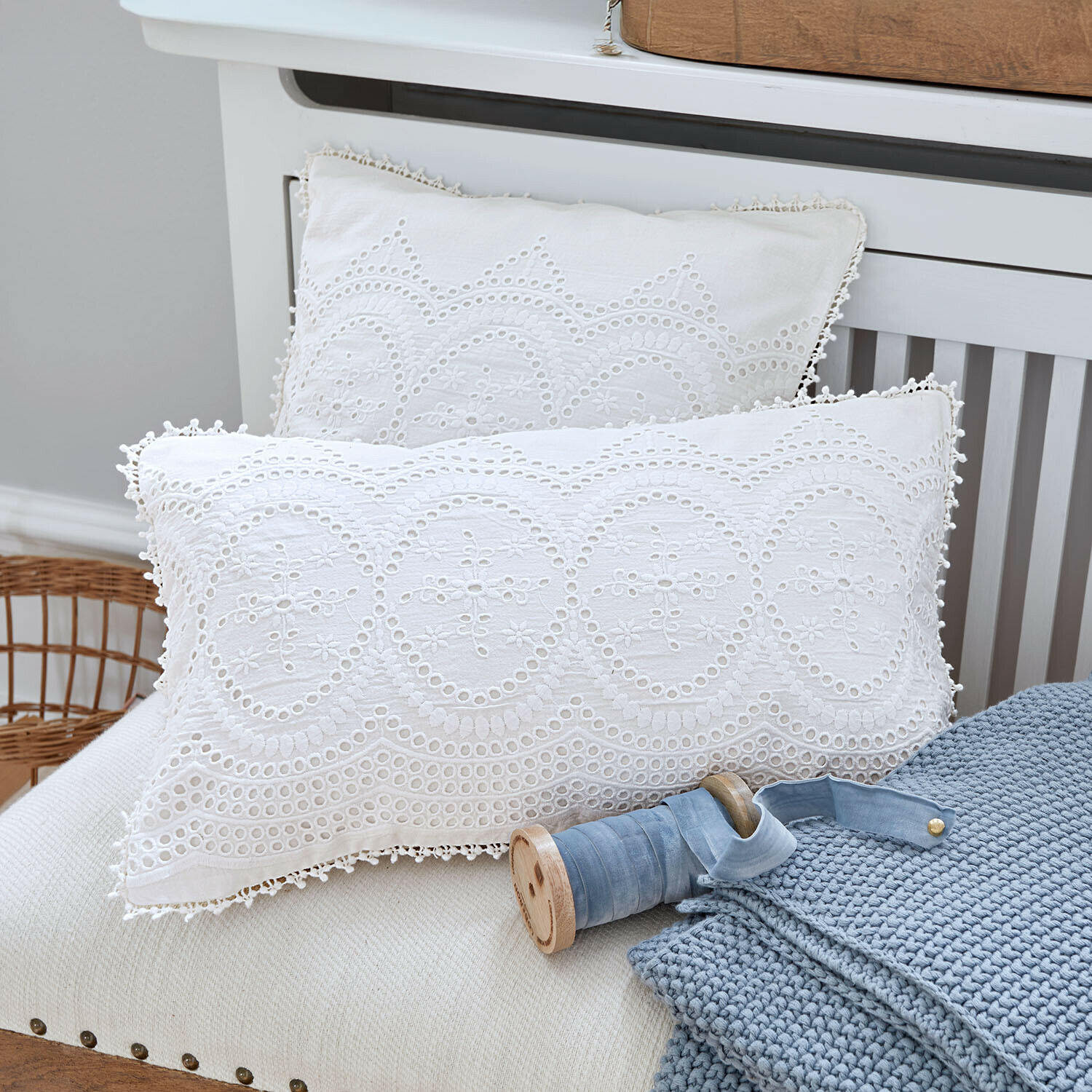 Cuscini bianchi in cotone con ricamo traforato su divano con coperta blu lavorata a maglia