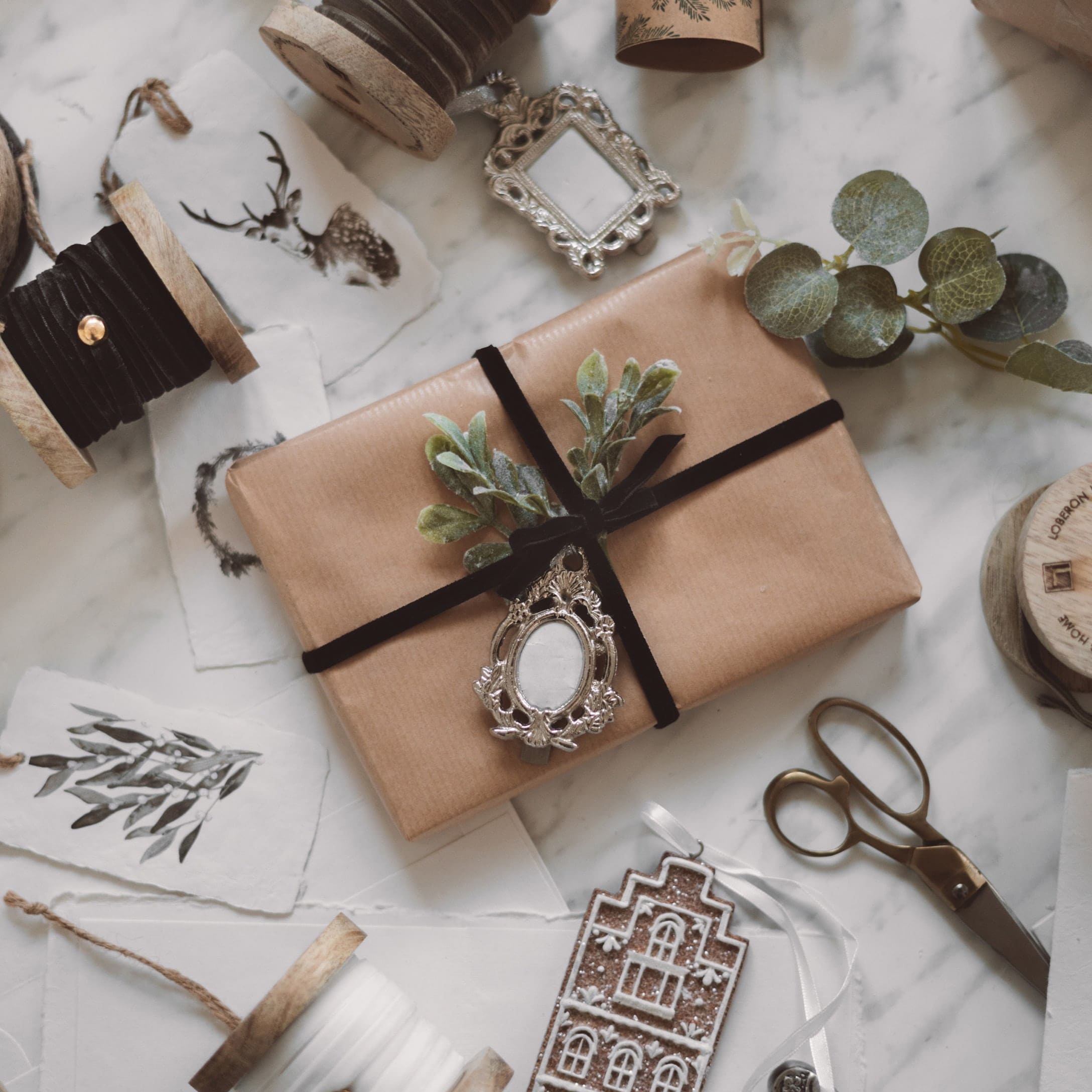 Regalo avvolto in carta marrone con nastro nero e foglie verdi su sfondo in marmo con decorazioni