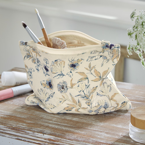 Beauty case beige in tessuto con motivo floreale e pennelli da trucco su tavolo in legno