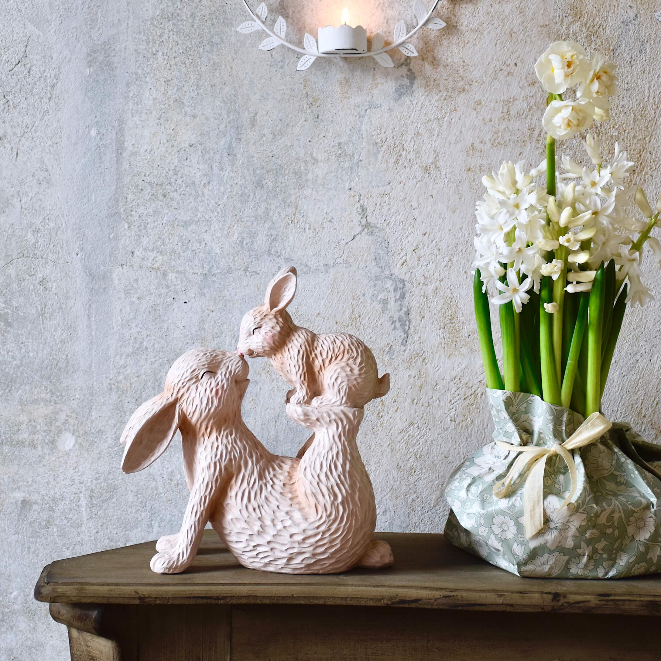 Scultura rosa in resina di due conigli su tavolo in legno con fiori in vaso pastello