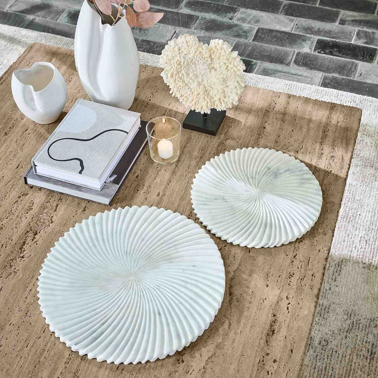 Due piastre decorative bianche in marmo con motivo ondulato su tavolo beige con libri e candela