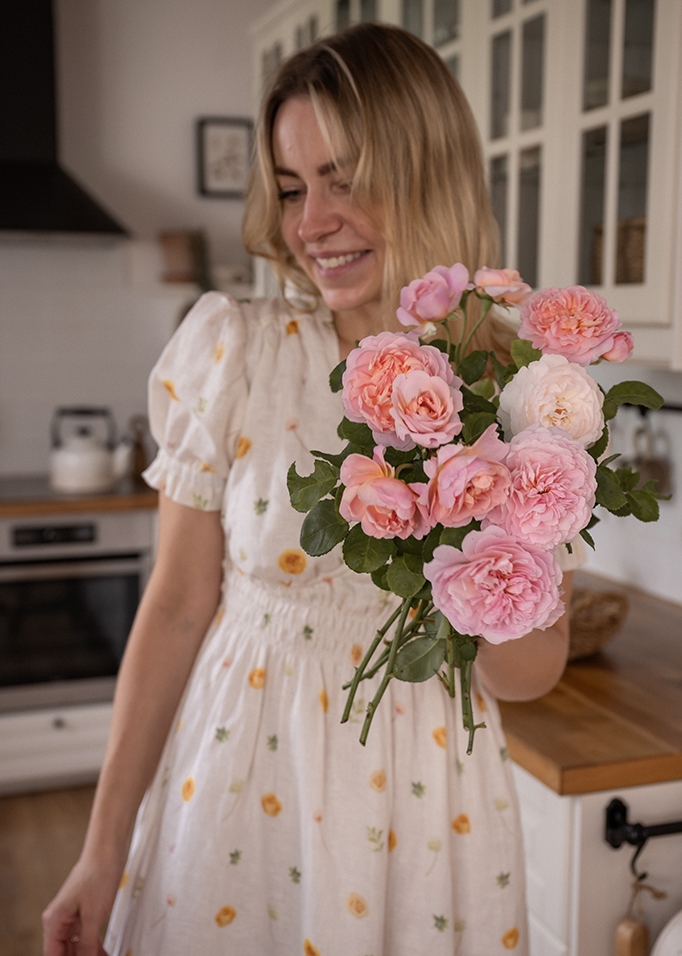Donna in abito chiaro che tiene un mazzo di rose rosa in cucina, decorazione floreale naturale