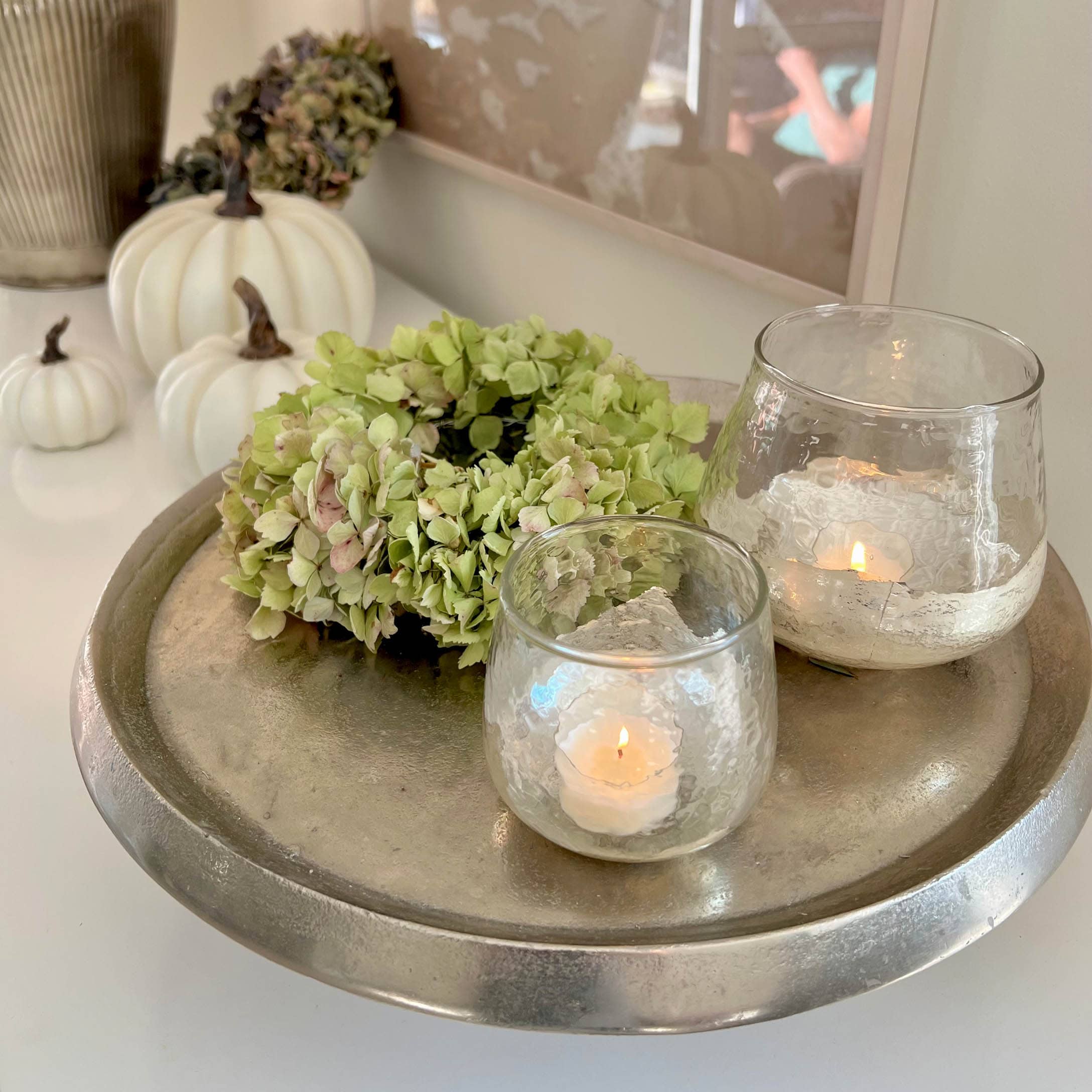Vassoio decorativo argentato con corona verde e due portacandele in vetro con candele bianche