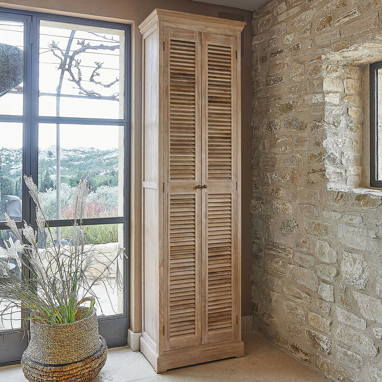 Armadio alto in legno naturale con ante a persiana in interno rustico con parete in pietra