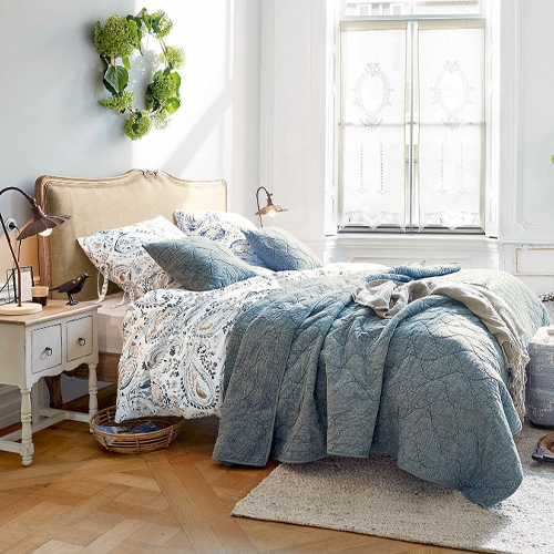 Camera accogliente con trapunta blu trapuntata e biancheria da letto decorata su letto con testiera beige