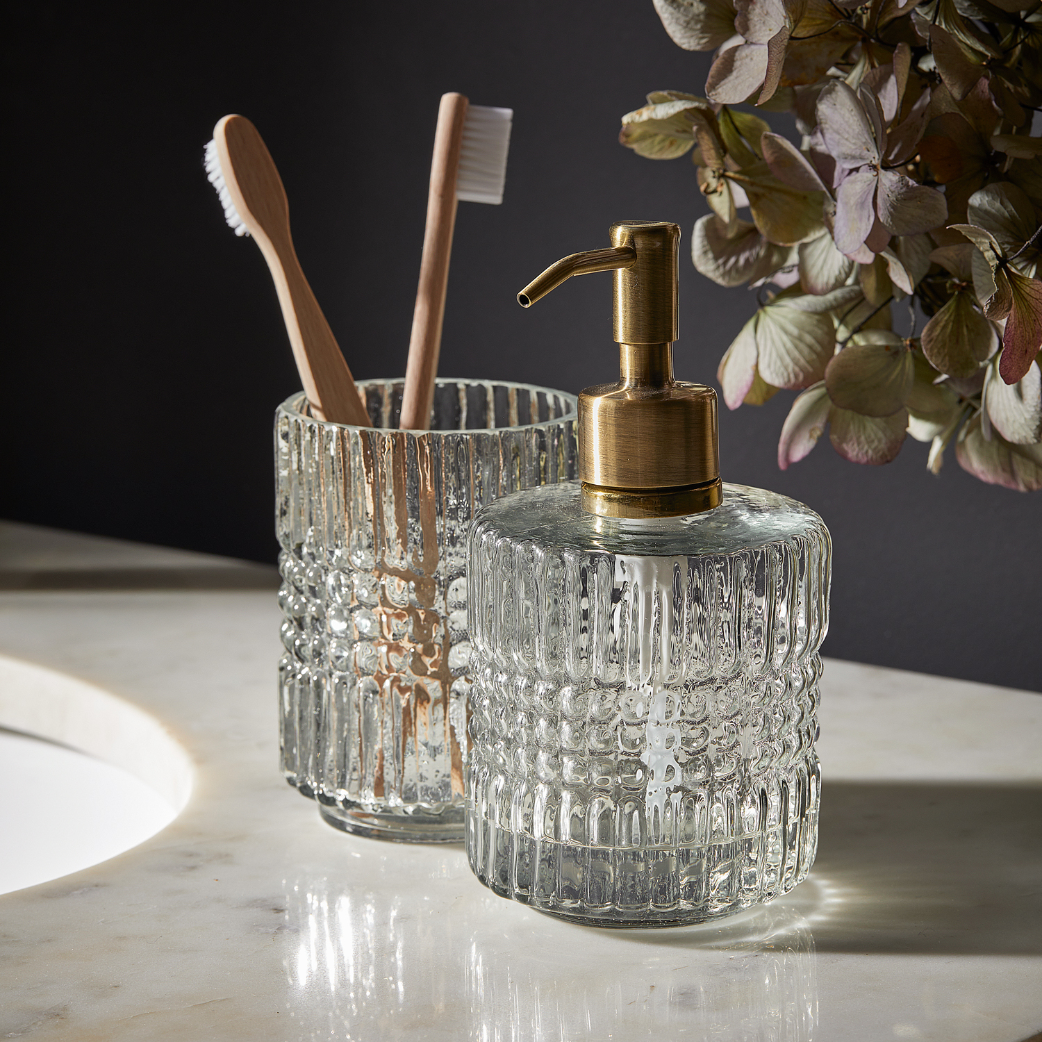 Dispenser per sapone in vetro con pompa in ottone e bicchiere in vetro per spazzolini su piano in marmo