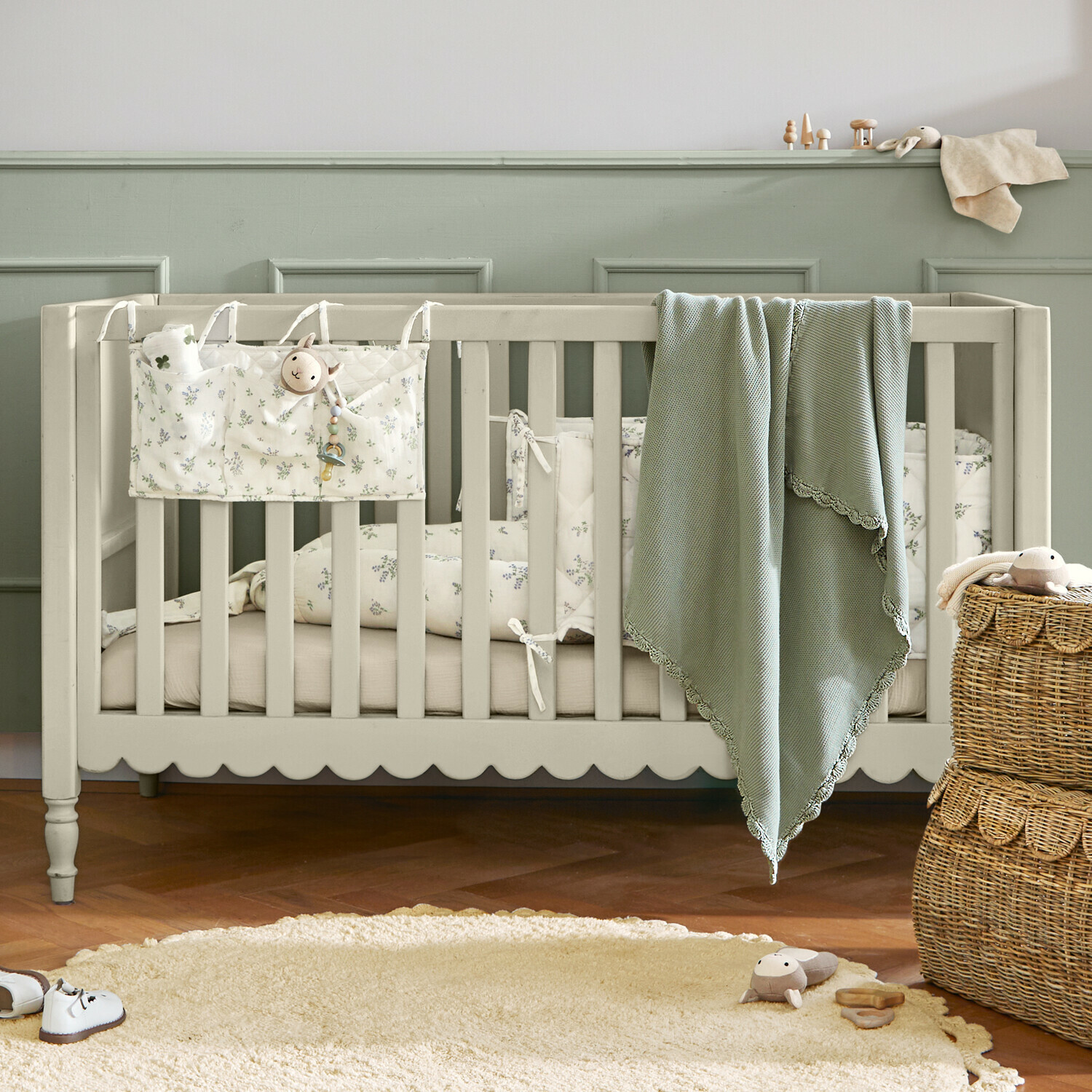 Lettino per neonati Leily Lettino per bambini in legno beige con coperta verde e biancheria da letto floreale in stanza accogliente