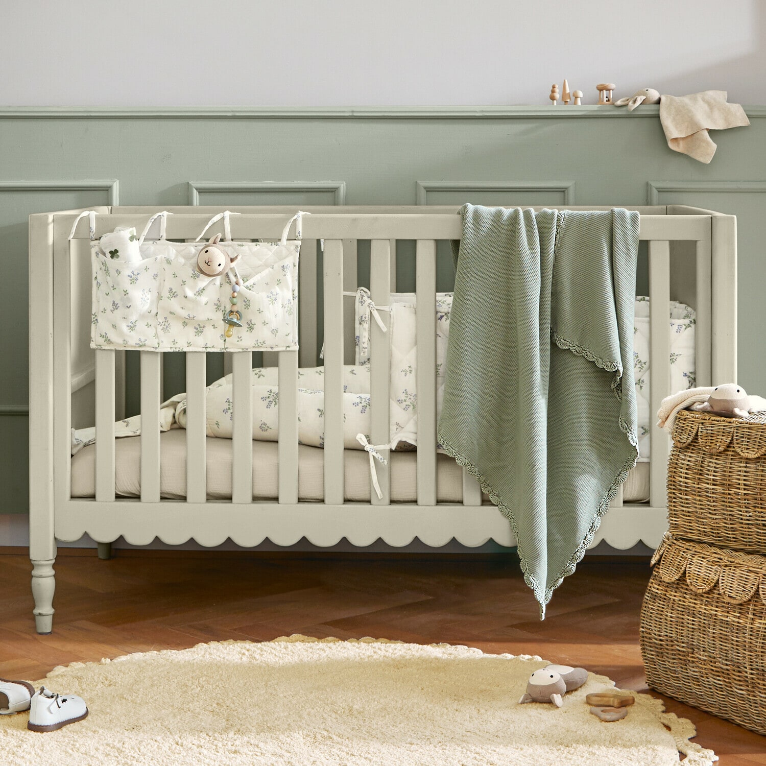 Lettino per neonati Leily Lettino per bambini in legno beige con coperta verde e biancheria da letto floreale in stanza accogliente