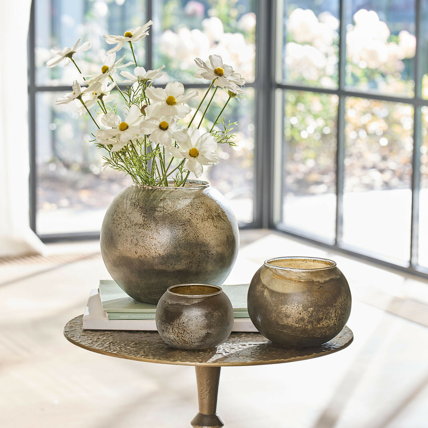 Set di tre vasi rotondi in vetro color oro antico su tavolo con fiori e libri