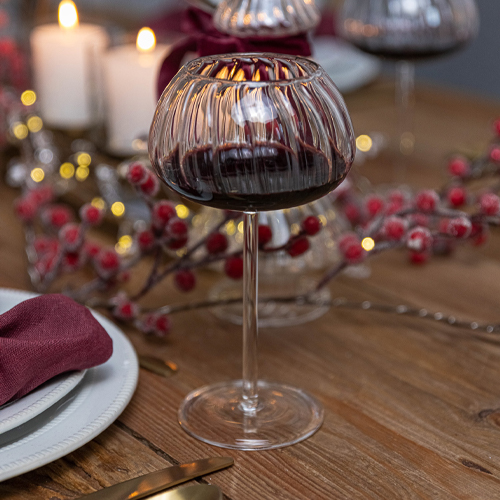 Bicchiere da vino in vetro scuro scanalato con gambo trasparente su tavolo in legno con decorazioni festive