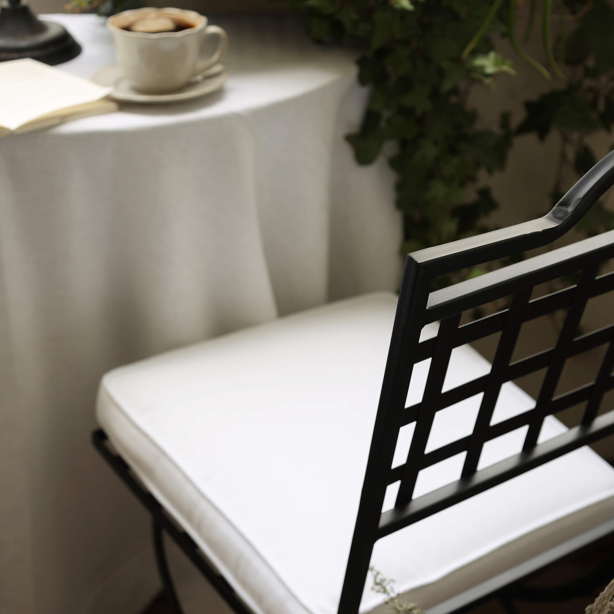 Sedia in metallo nero con cuscino bianco vicino a tavolo con tazza di caffè e piante verdi sul balcone