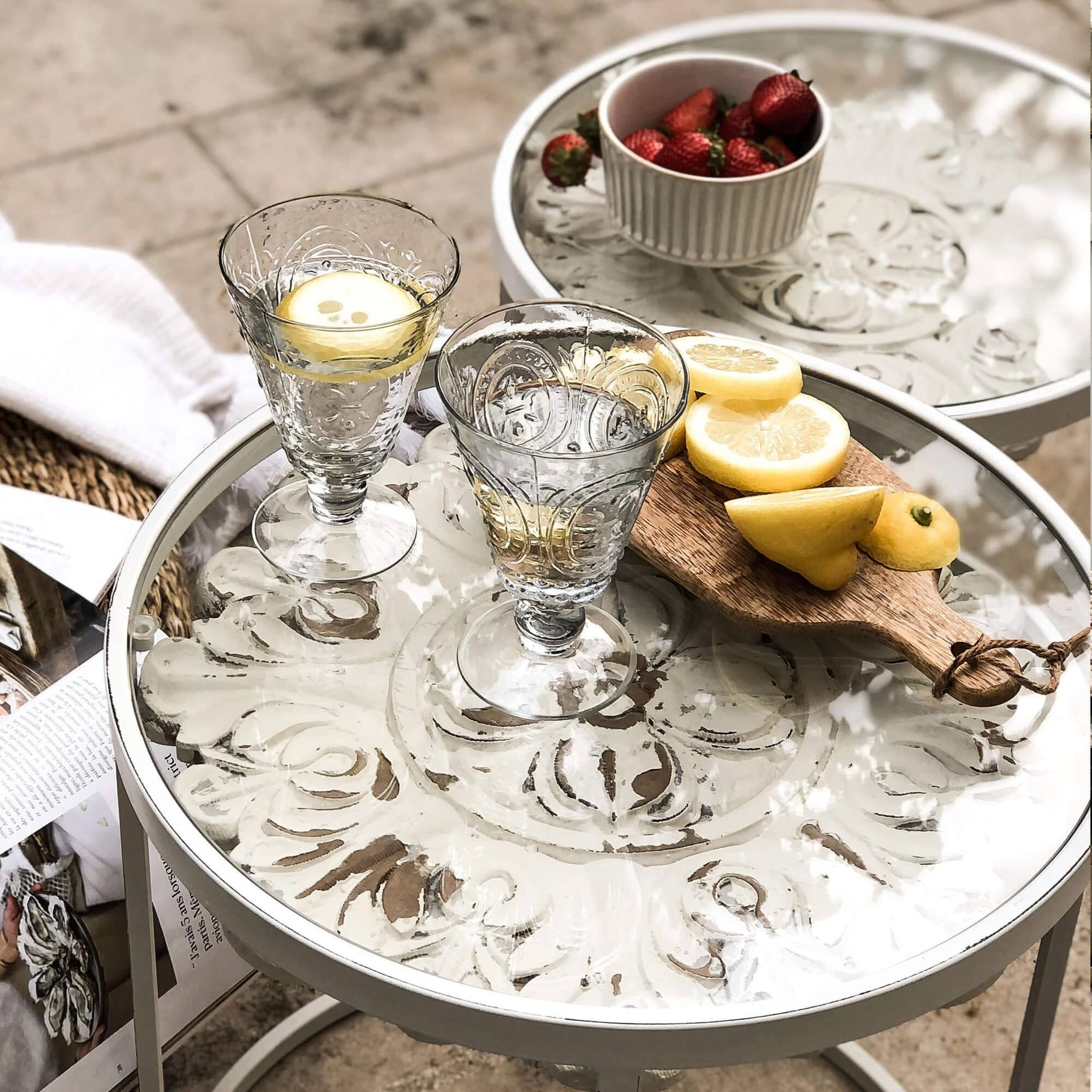 Bicchieri di vetro con acqua e limone su tavolino bianco in metallo con piano decorativo