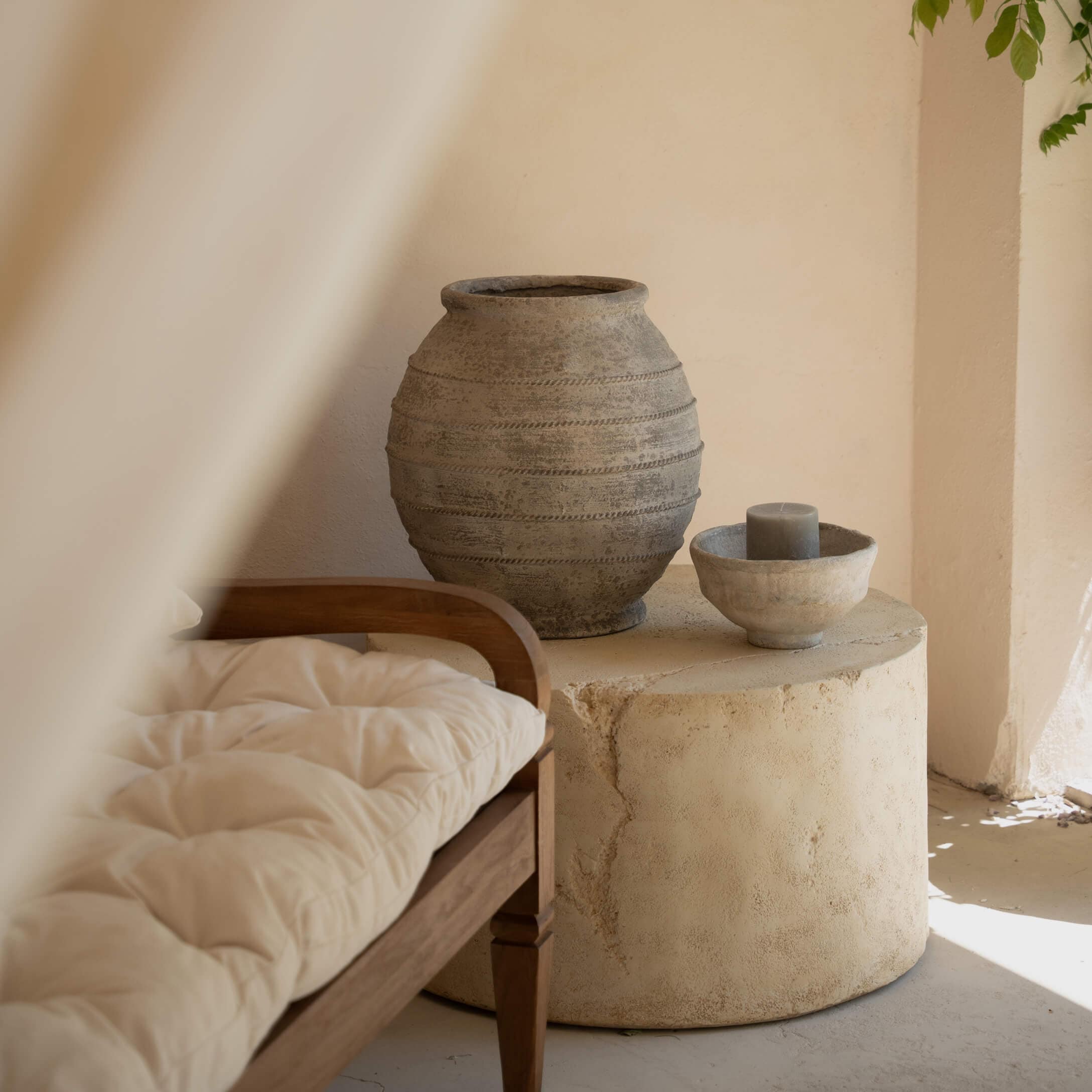 Tavolo rotondo in pietra con vaso in ceramica grigia e candela in interno luminoso con panca in legno
