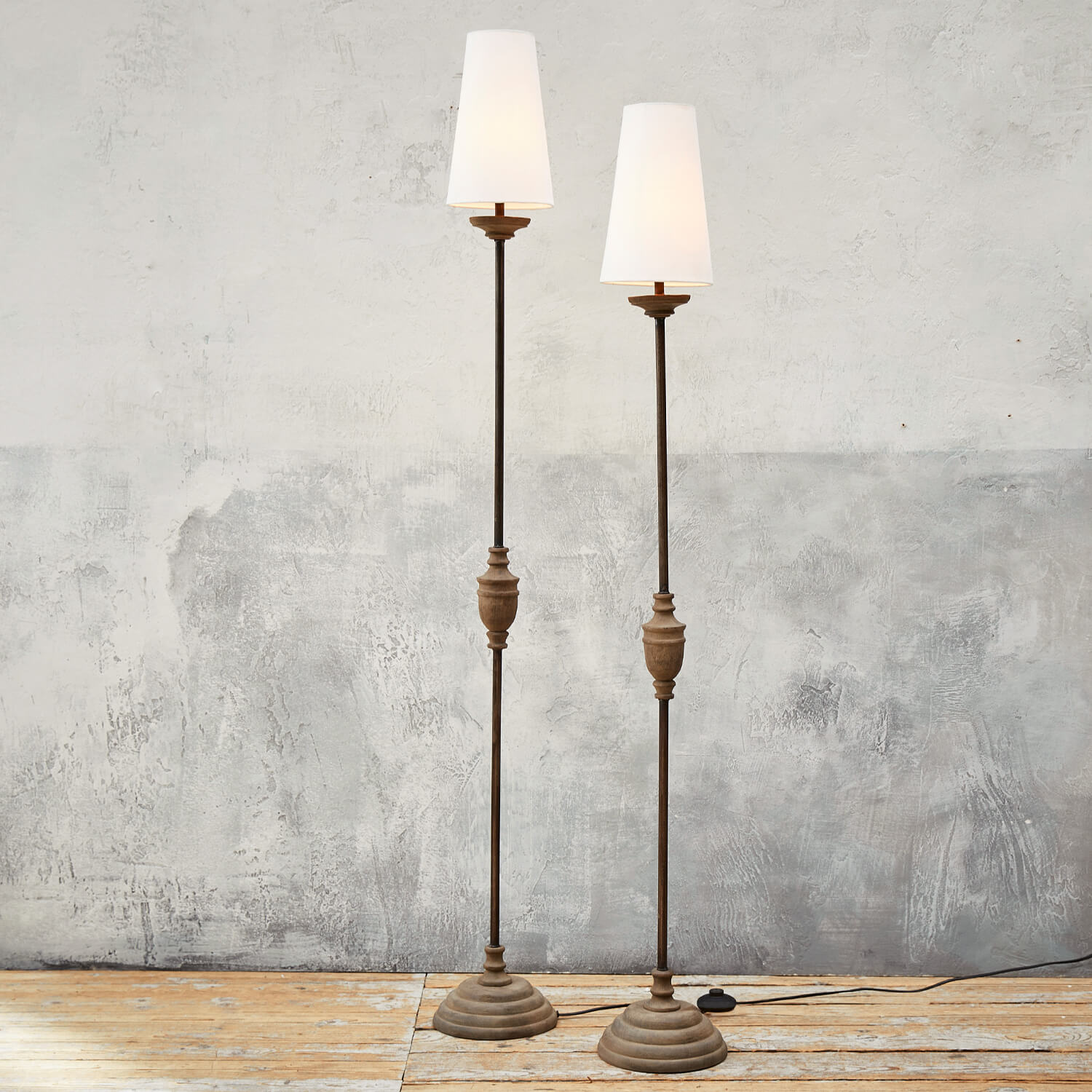Due lampade da terra alte con base in metallo e paralumi bianchi su pavimento in legno chiaro