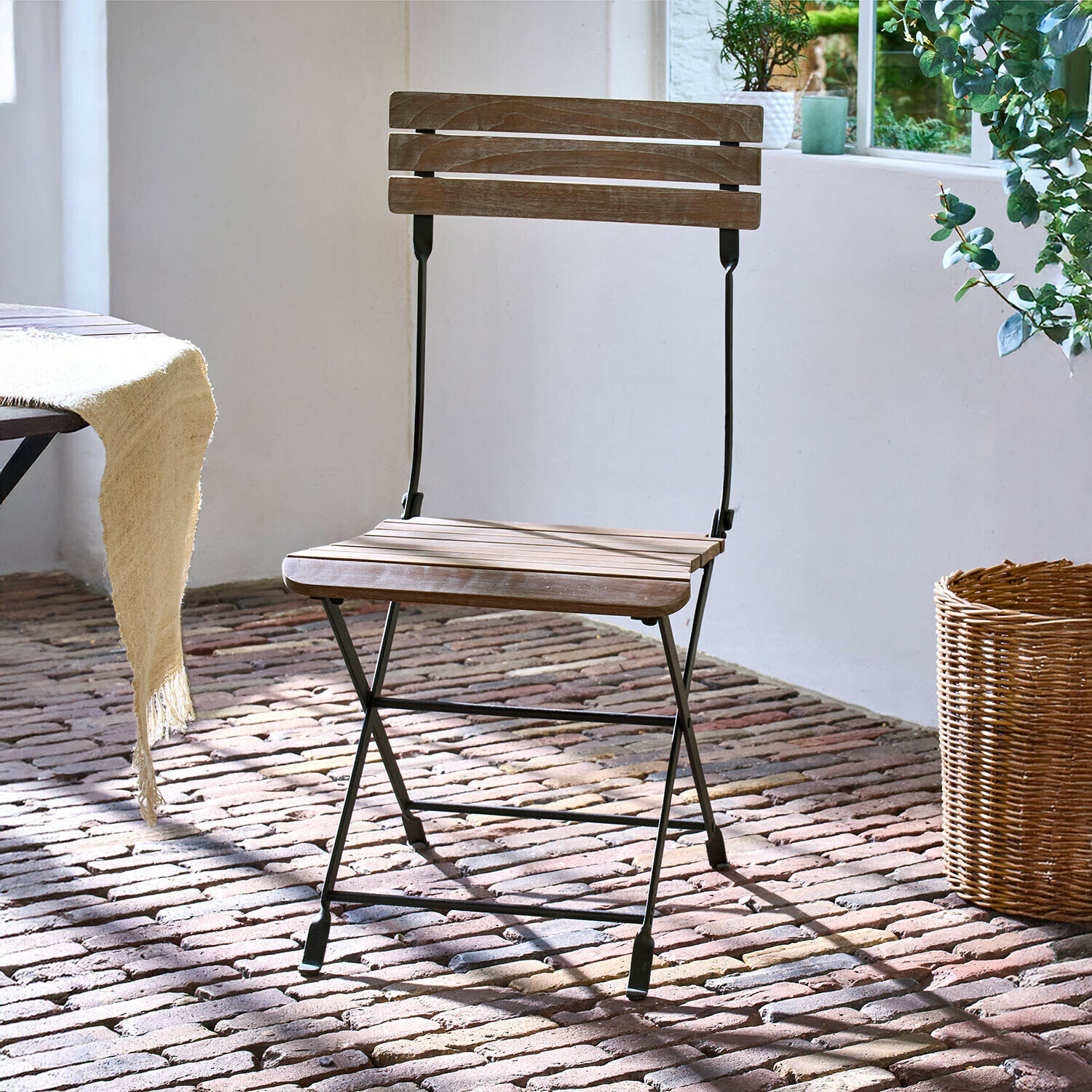 Sedia Arémont Sedia pieghevole in legno con struttura metallica nera su pavimento in mattoni alla luce naturale