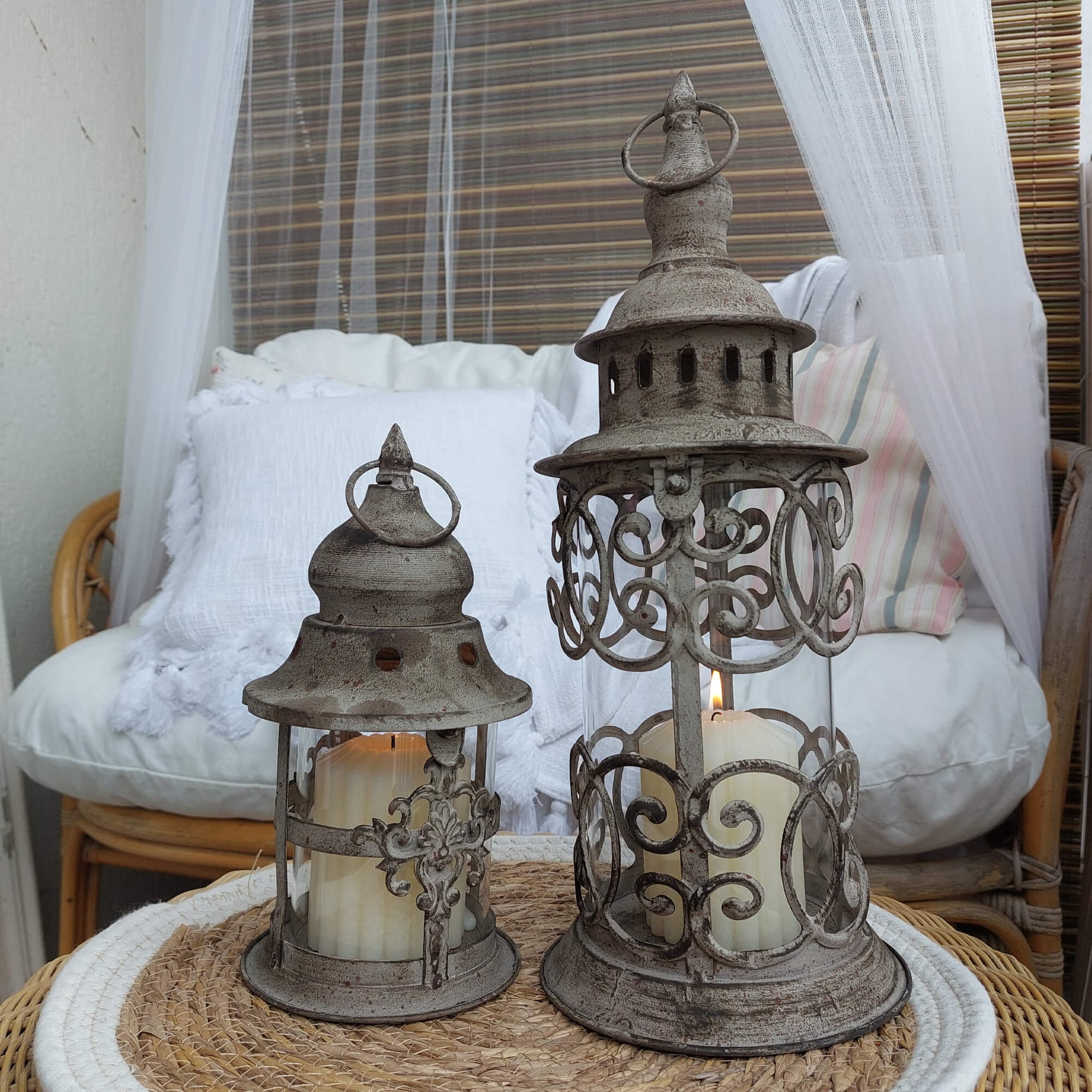 Due lanterne vintage in metallo grigio con candele bianche su tavolo in vimini