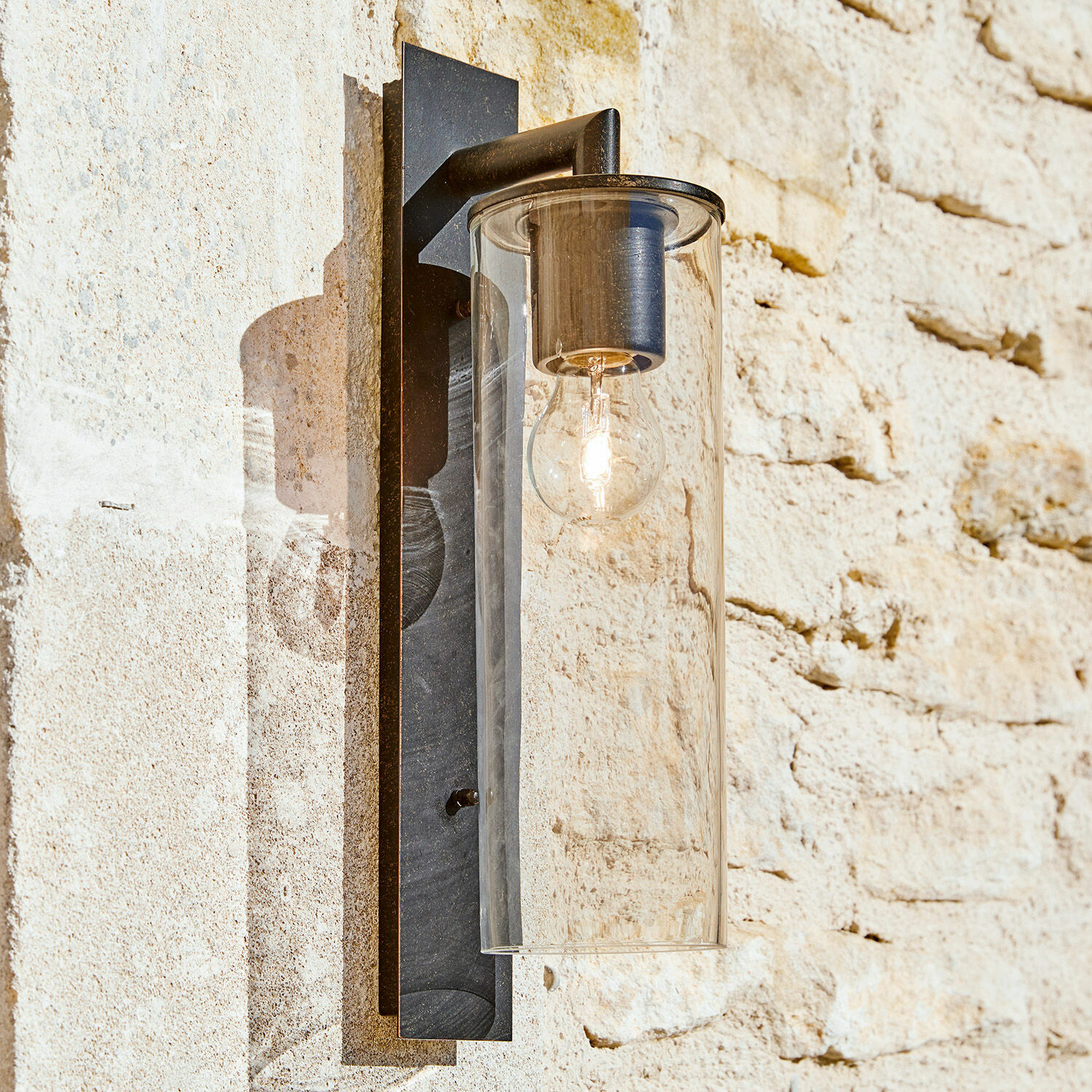 Lampada da parete per esterni Clisson Applique da parete in metallo nero con paralume in vetro trasparente su muro di pietra chiara