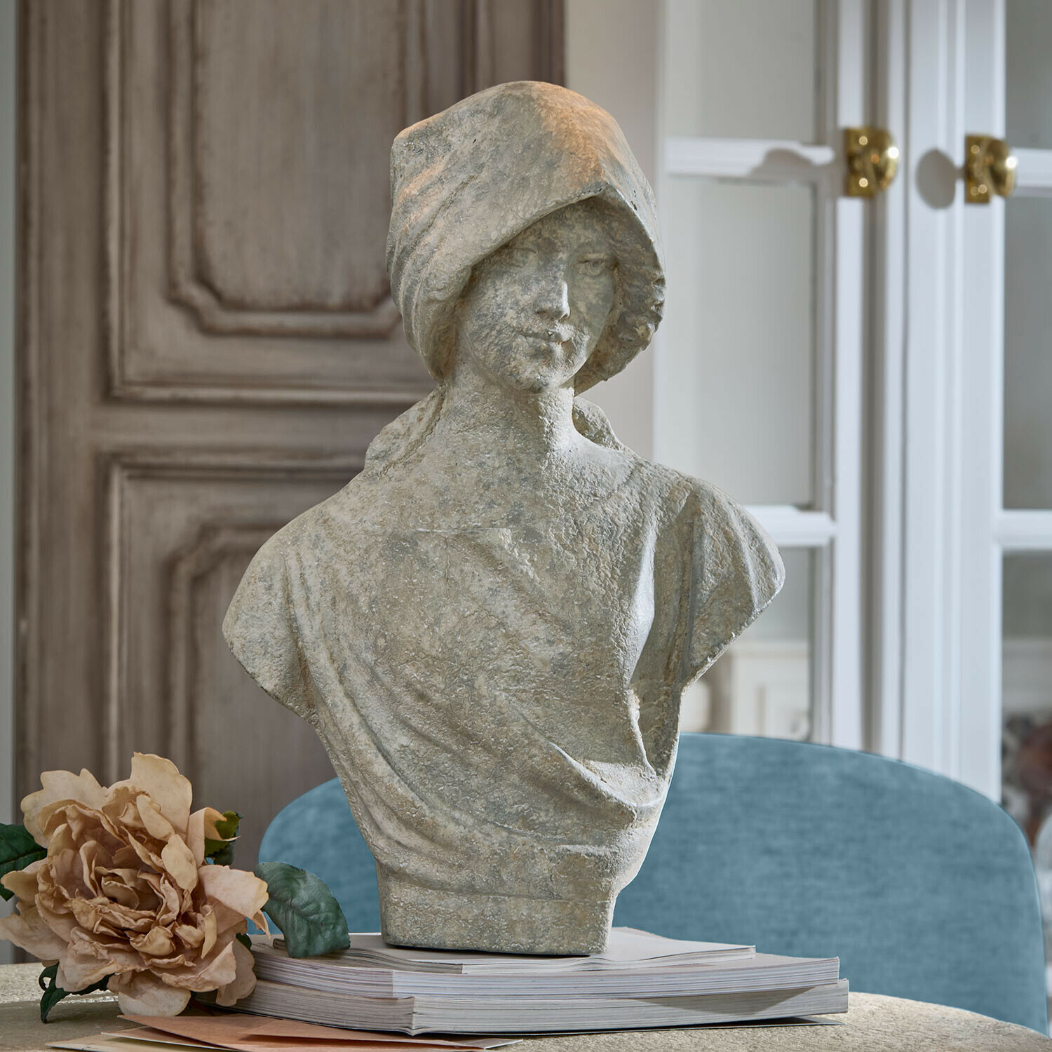 Busto Mireline Busto femminile in pietra grigia su libri con fiore decorativo accanto in ambiente elegante