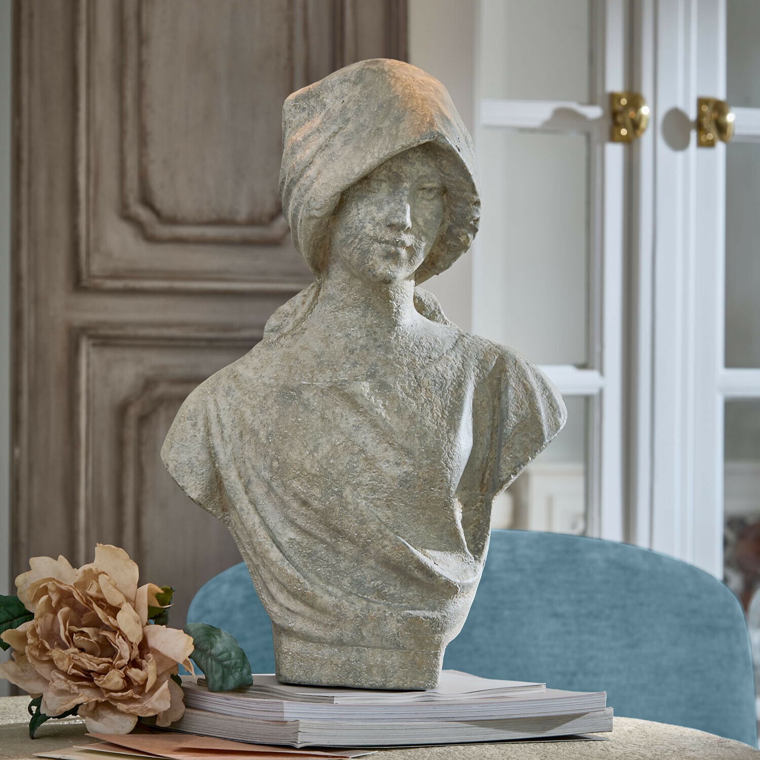 Busto Mireline Busto femminile in pietra grigia su libri con fiore decorativo accanto in ambiente elegante