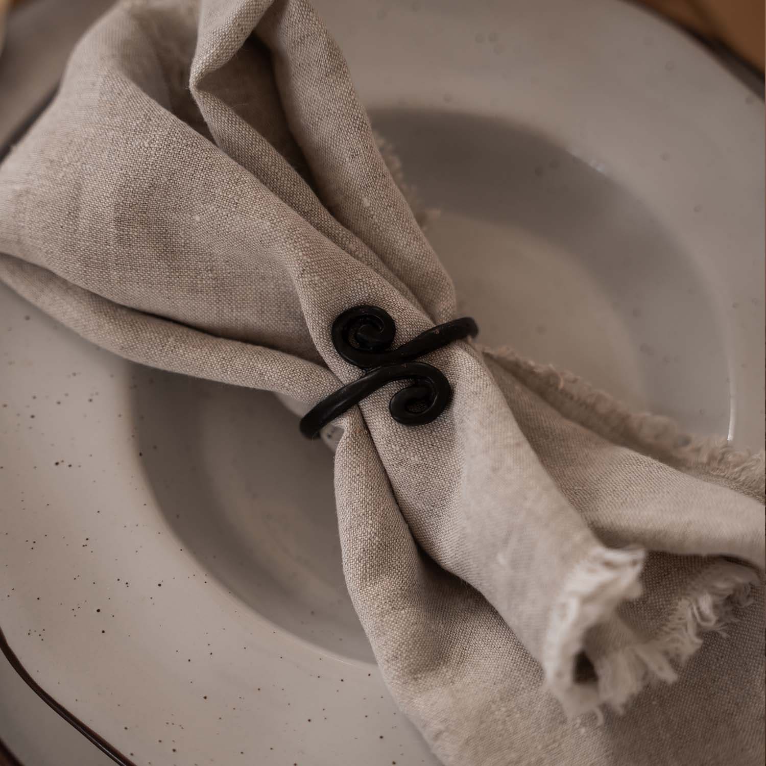 Tovagliolo in lino beige con anello in metallo nero su piatto chiaro