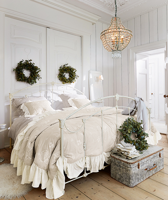 Camera da letto con letto in metallo crema, biancheria da letto beige con volant e corone decorative verdi su porte bianche