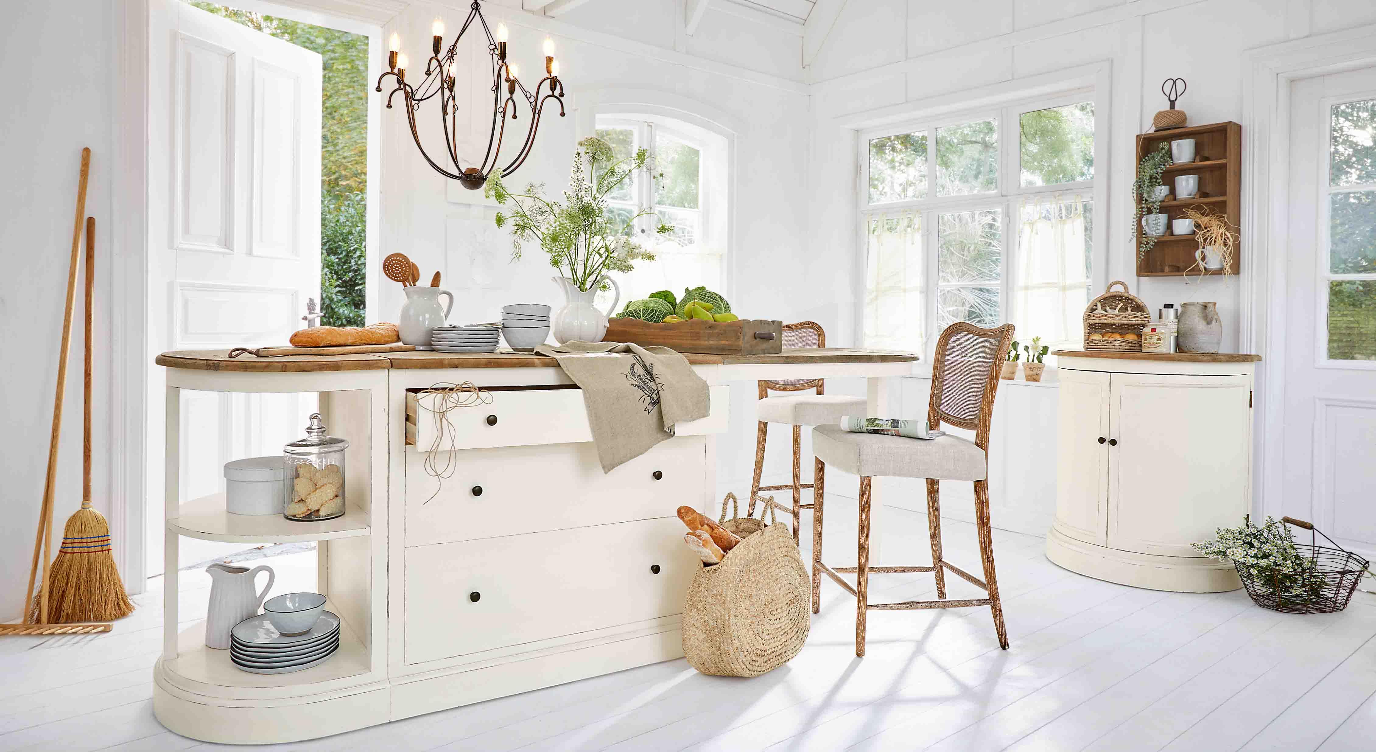 Cucina luminosa con isola bianca in legno e sedie in vimini, decorazioni naturali