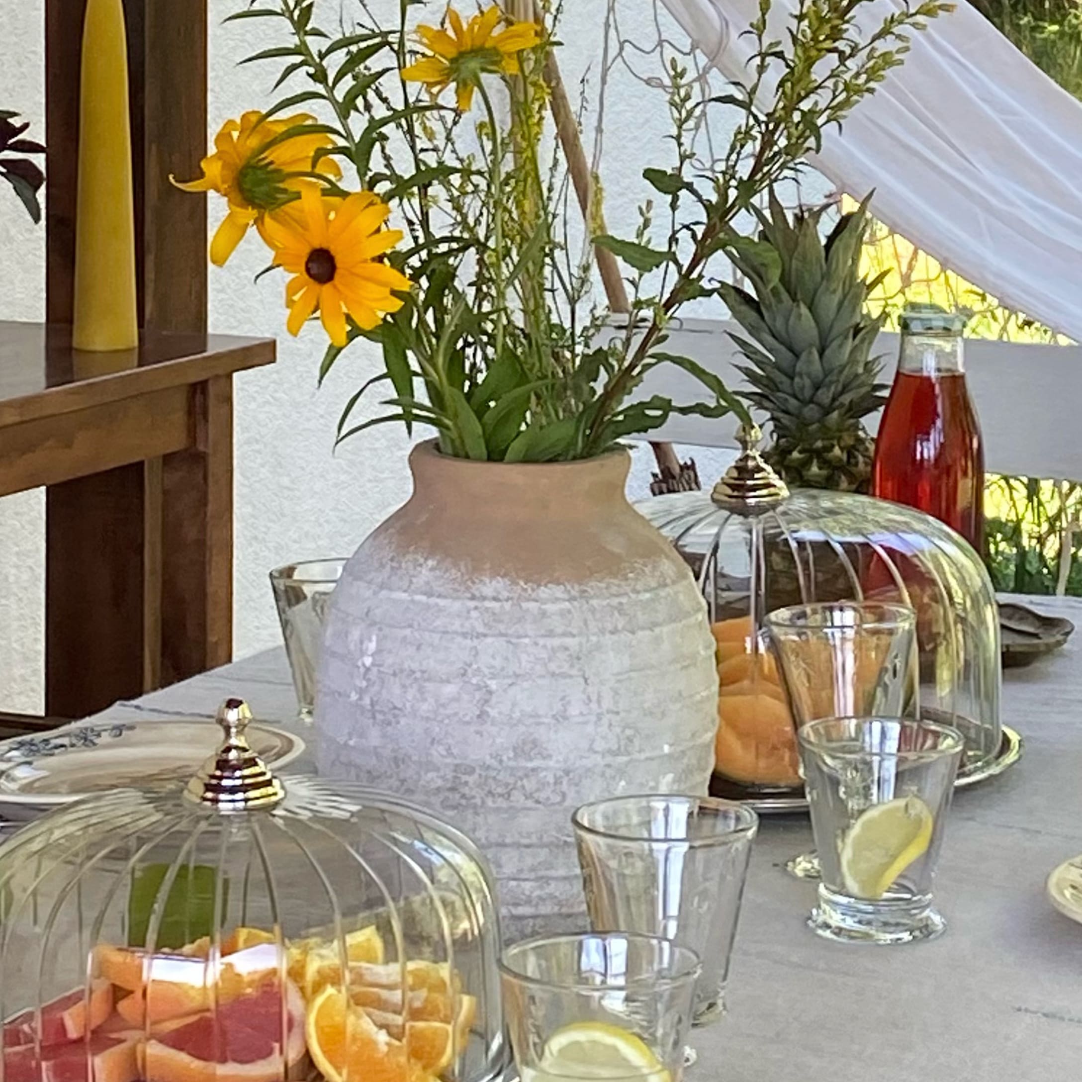 Vaso in ceramica bianca con fiori gialli su tavolo con frutta e bicchieri con limone