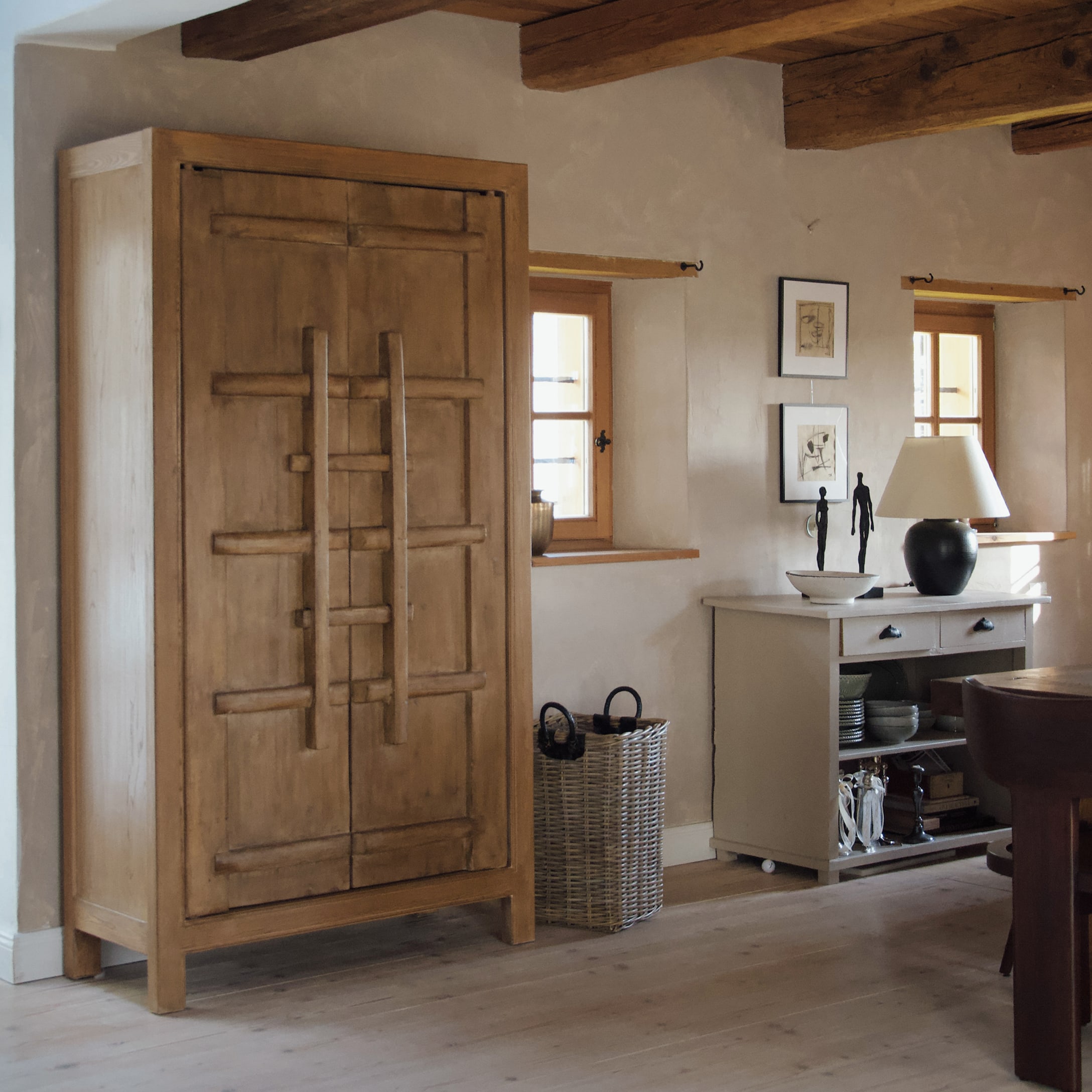 Armadio in legno colore naturale in interno rustico con cesta di vimini e cassettiera bianca