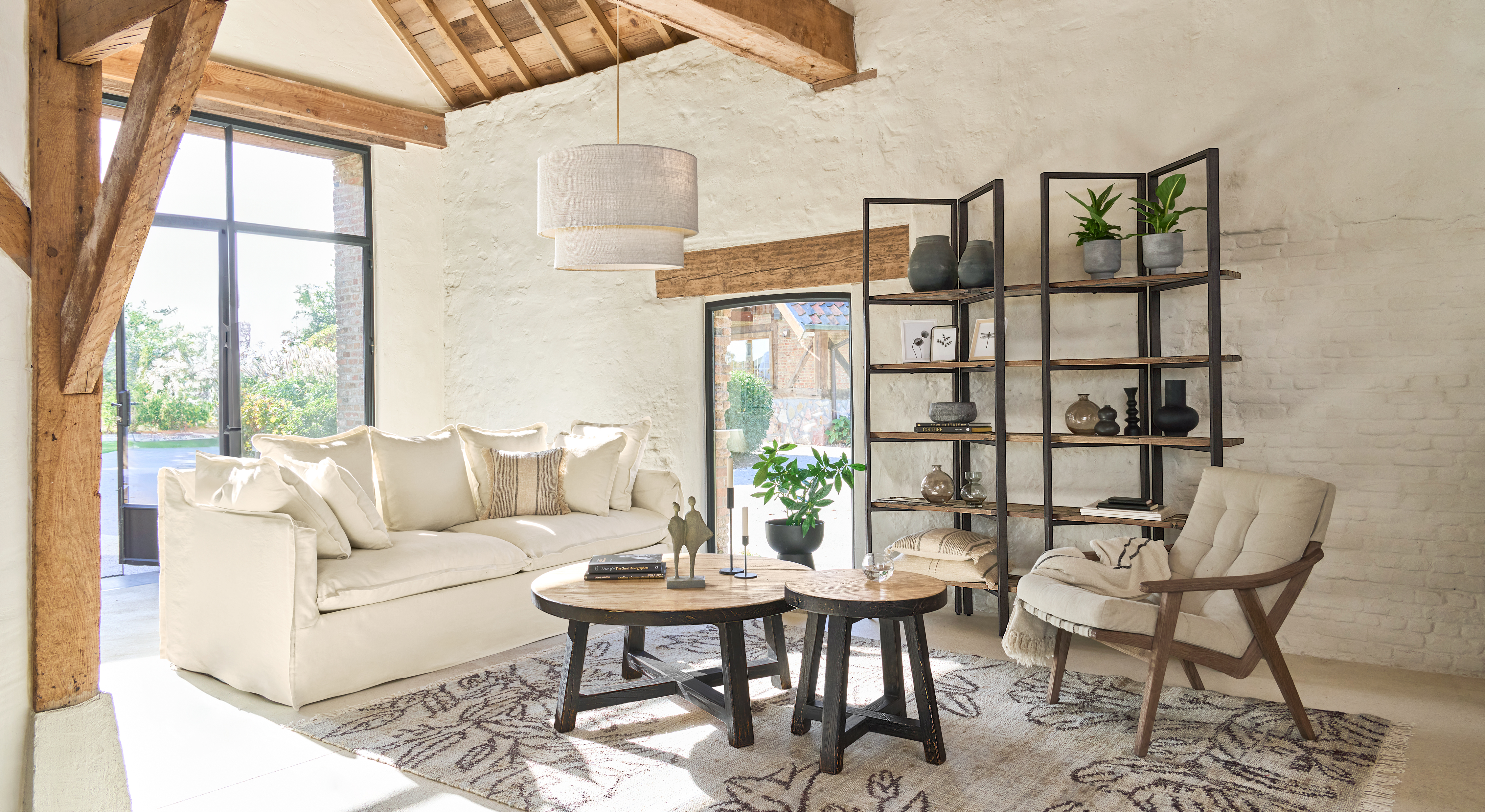 Soggiorno luminoso con divano bianco, tavolini in legno e scaffale in metallo e legno, stile naturale