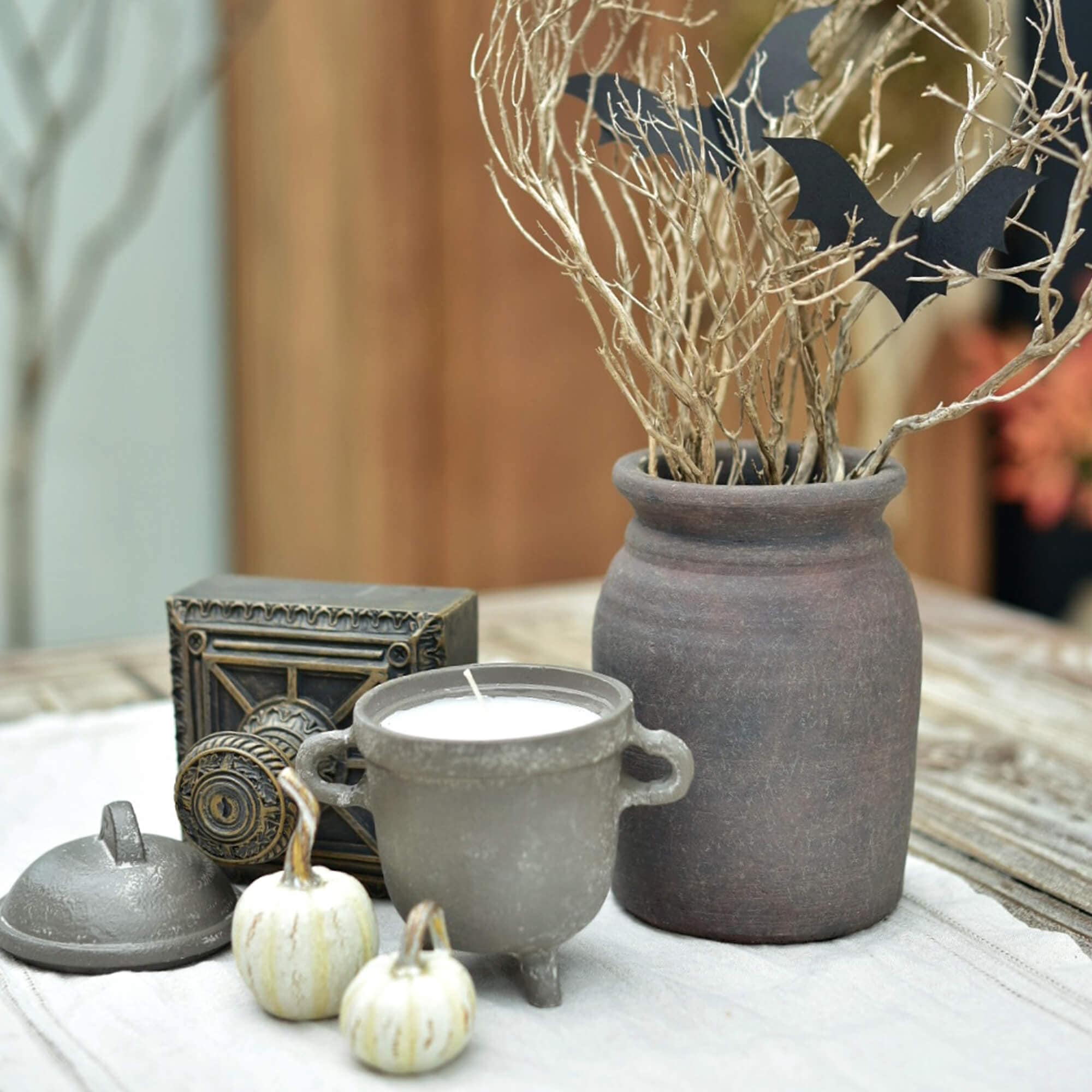 Set decorativo con candela in ceramica, vaso in terracotta e piccole zucche bianche su tavolo