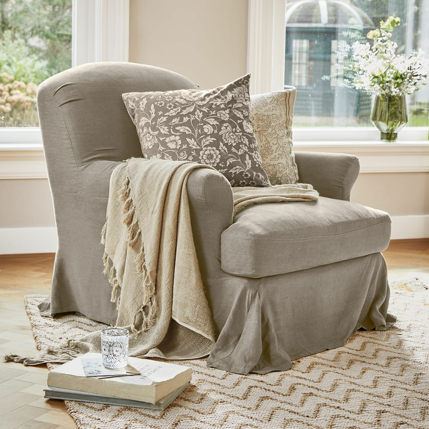 Poltrona Vionnique Poltrona beige in tessuto con cuscini decorativi e coperta su tappeto chiaro in soggiorno