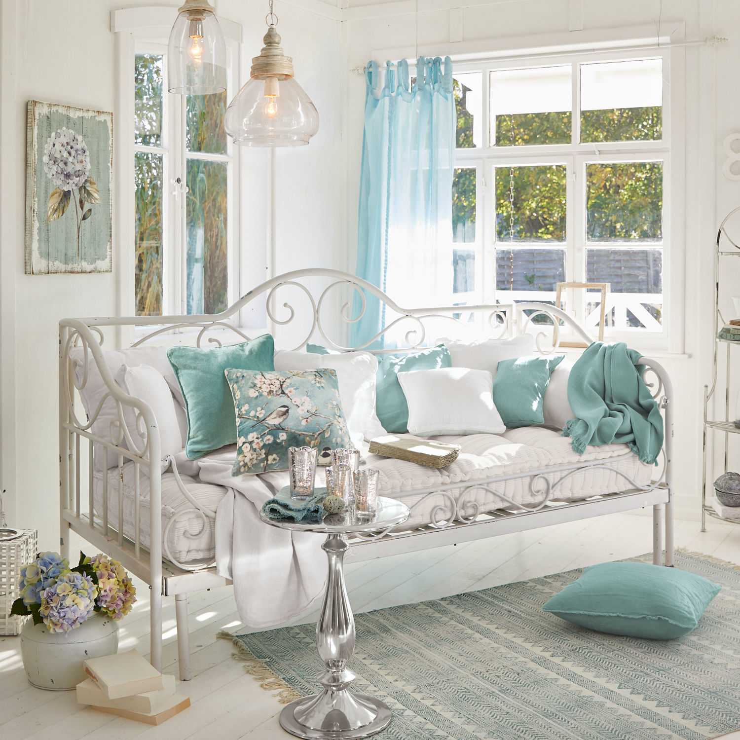 Divano letto Maditha Divano in metallo bianco con cuscini morbidi e dettagli turchesi in soggiorno luminoso con grande finestra
