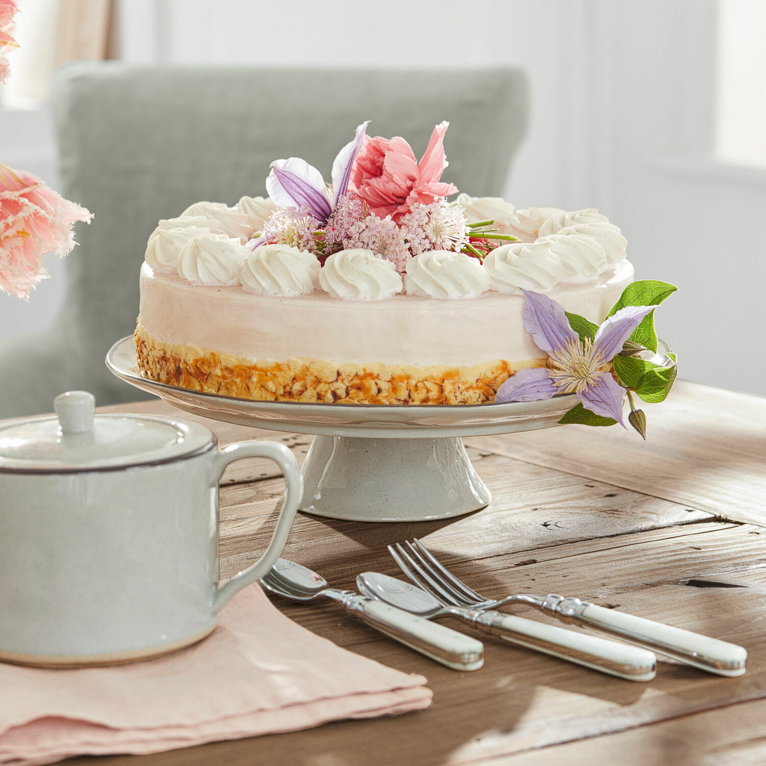 Centrotavola Biarré Torta su alzata in ceramica con crema e fiori, posate con manici bianchi su tavolo in legno