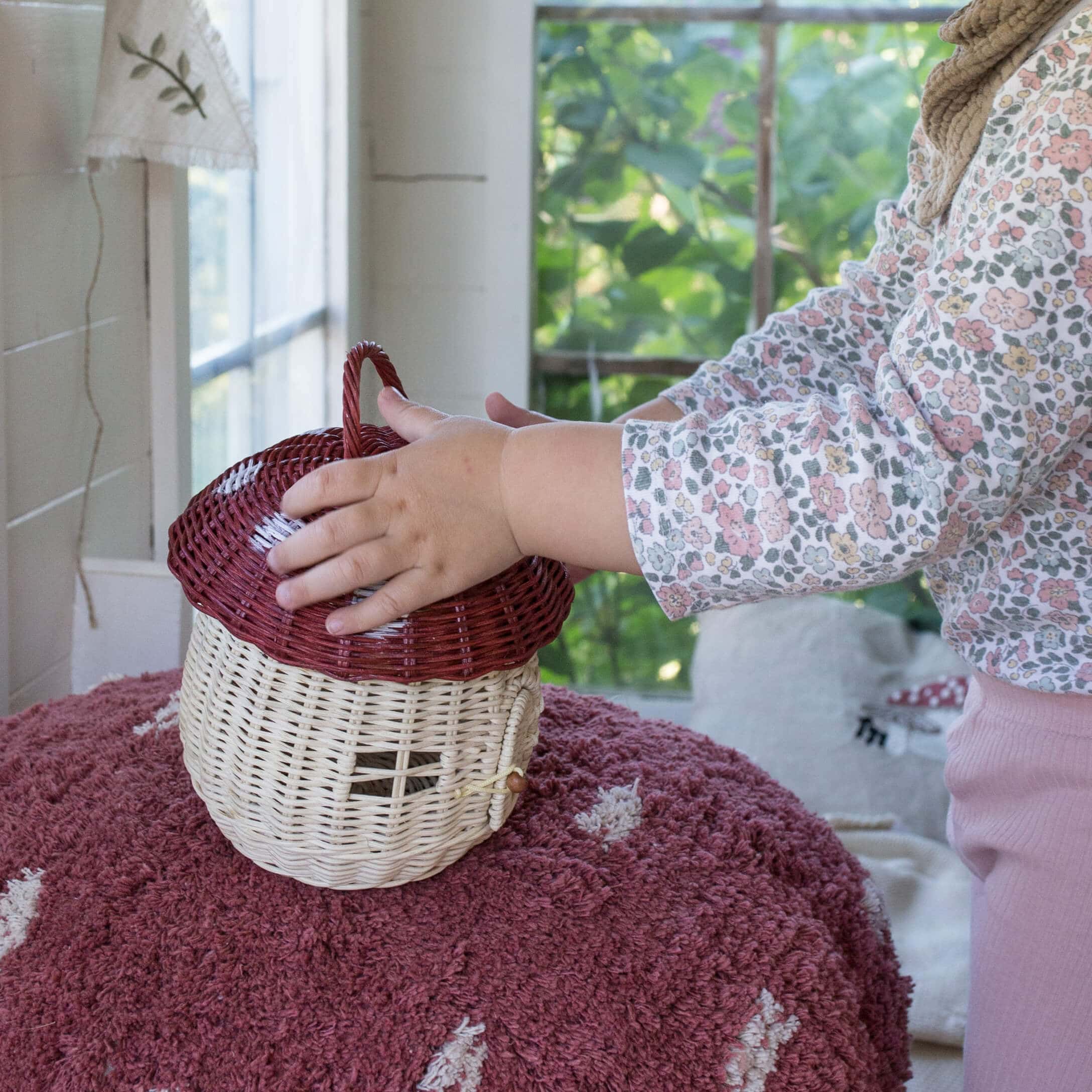 Bambino tocca cesto in vimini a forma di fungo beige e rosso su tappeto rosa in casa