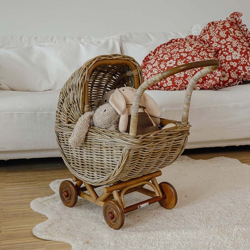 Carrozzina in vimini con ruote in legno e peluche in stanza luminosa con divano bianco