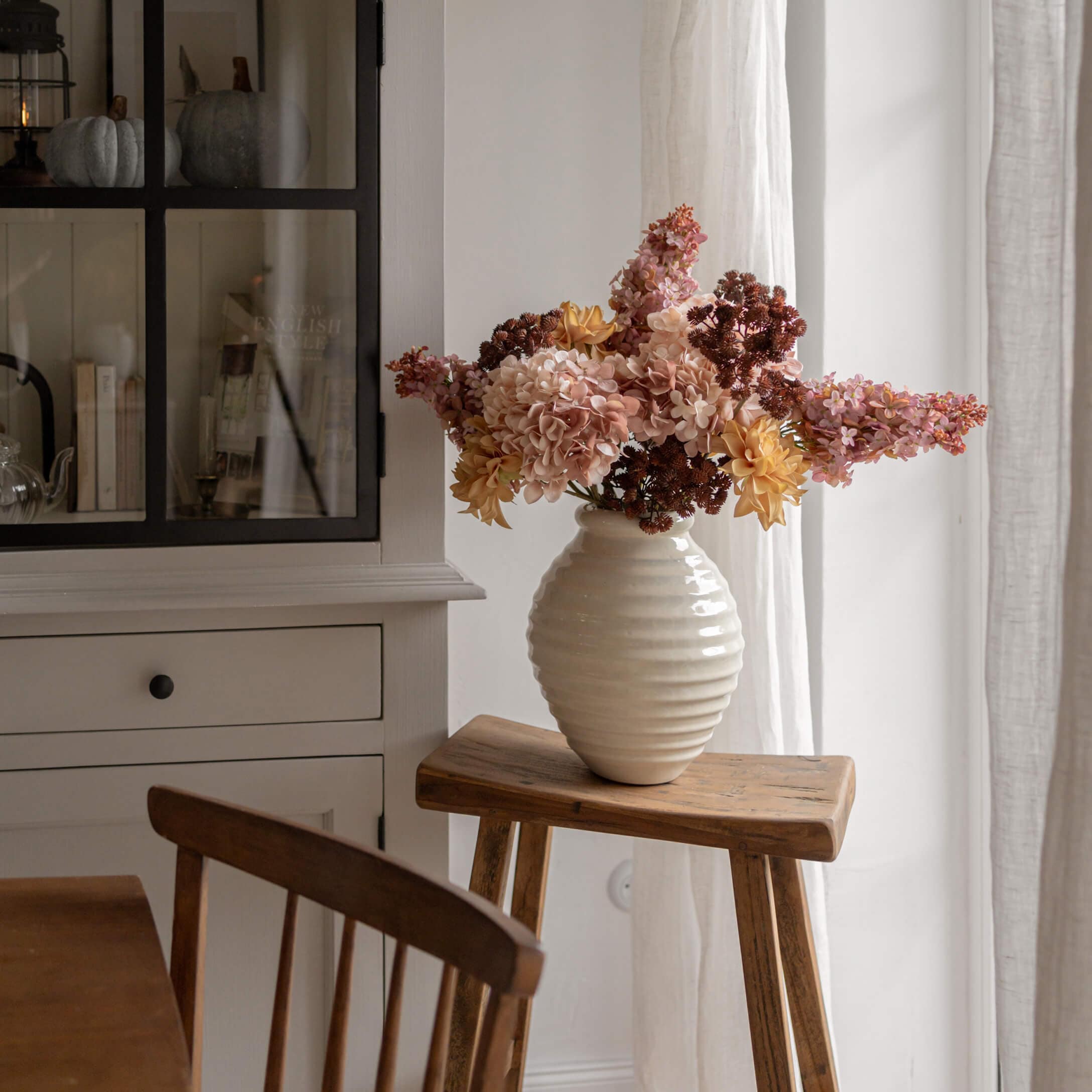 Vaso in alabastro bianco con fiori gialli e rosa su sgabello di legno in interno luminoso