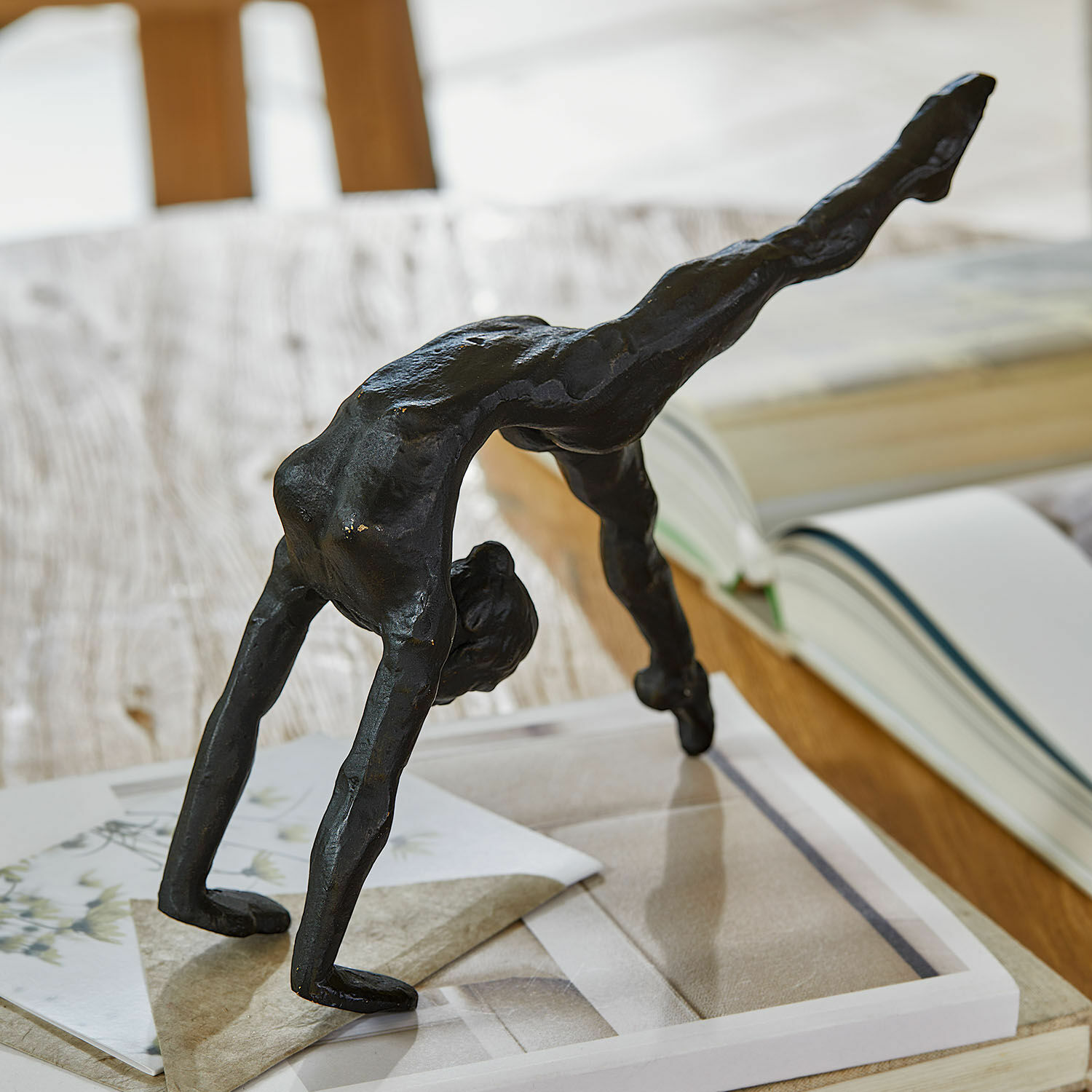 Statuina Zayrah Figura nera in metallo di acrobata in posizione ponte su tavolo con libri e carte