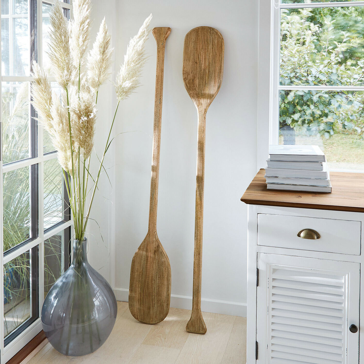 Due remi decorativi in legno in interno luminoso accanto a vaso grigio e mobile bianco