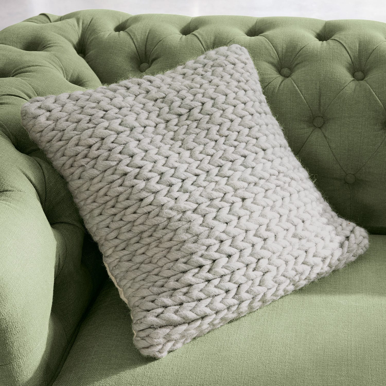 Copricuscino Limnia Cuscino beige a maglia grossa in lana morbida su divano verde trapuntato