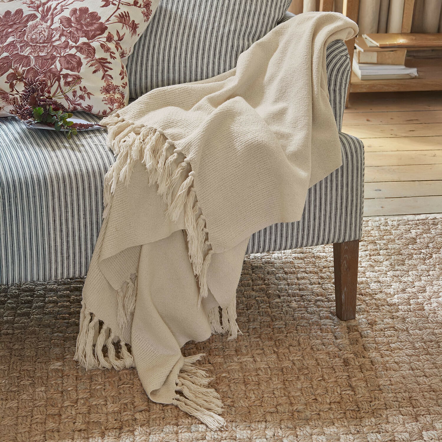 Coperta Skandira Coperta beige con frange in tessuto morbido su divano grigio a righe in ambiente accogliente