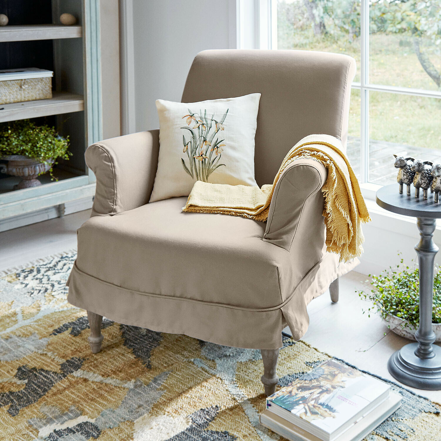 Poltrona Everleighs Poltrona beige in tessuto con cuscino floreale e coperta gialla in soggiorno luminoso con tappeto