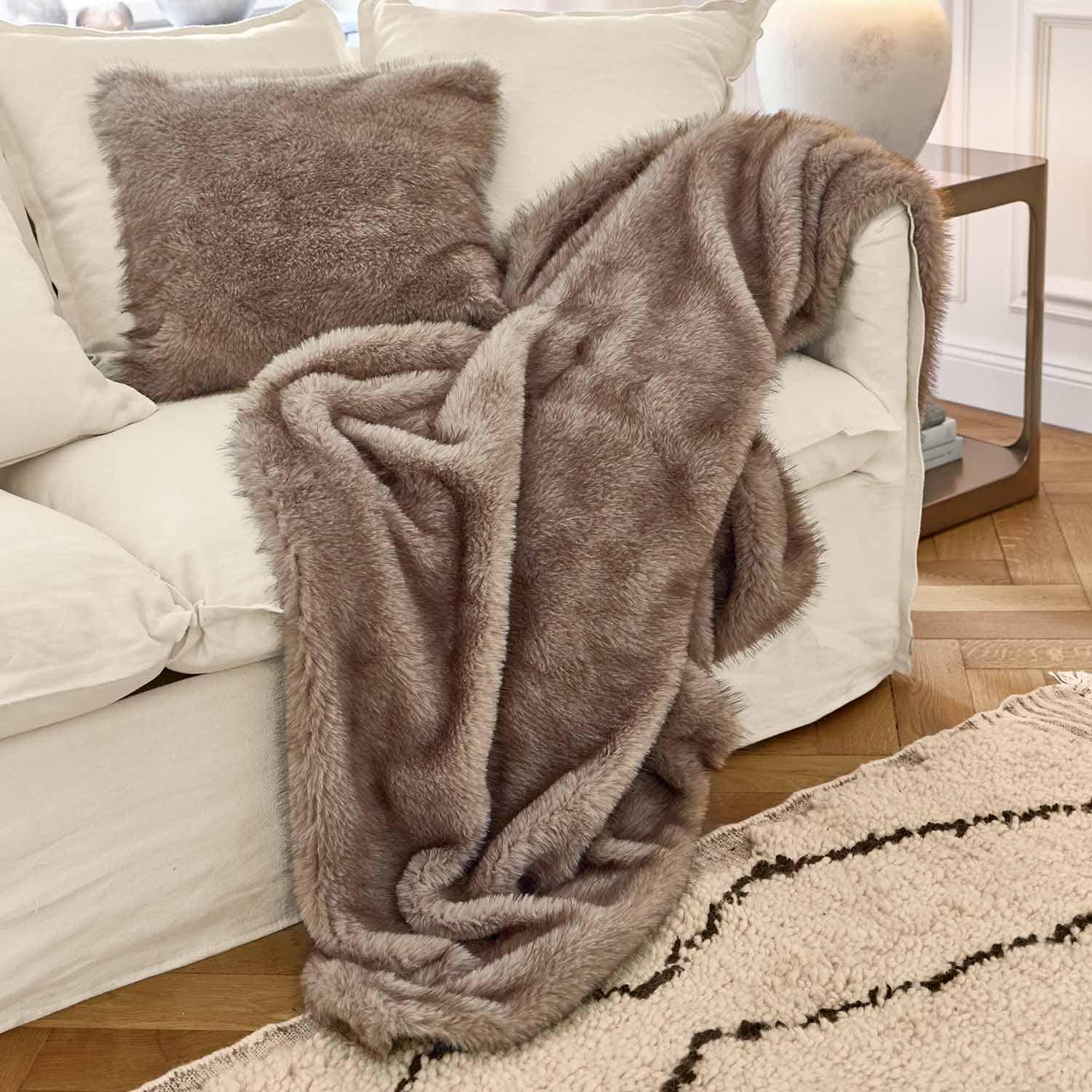 Coperta e cuscino in pelliccia sintetica marrone su divano bianco in soggiorno accogliente