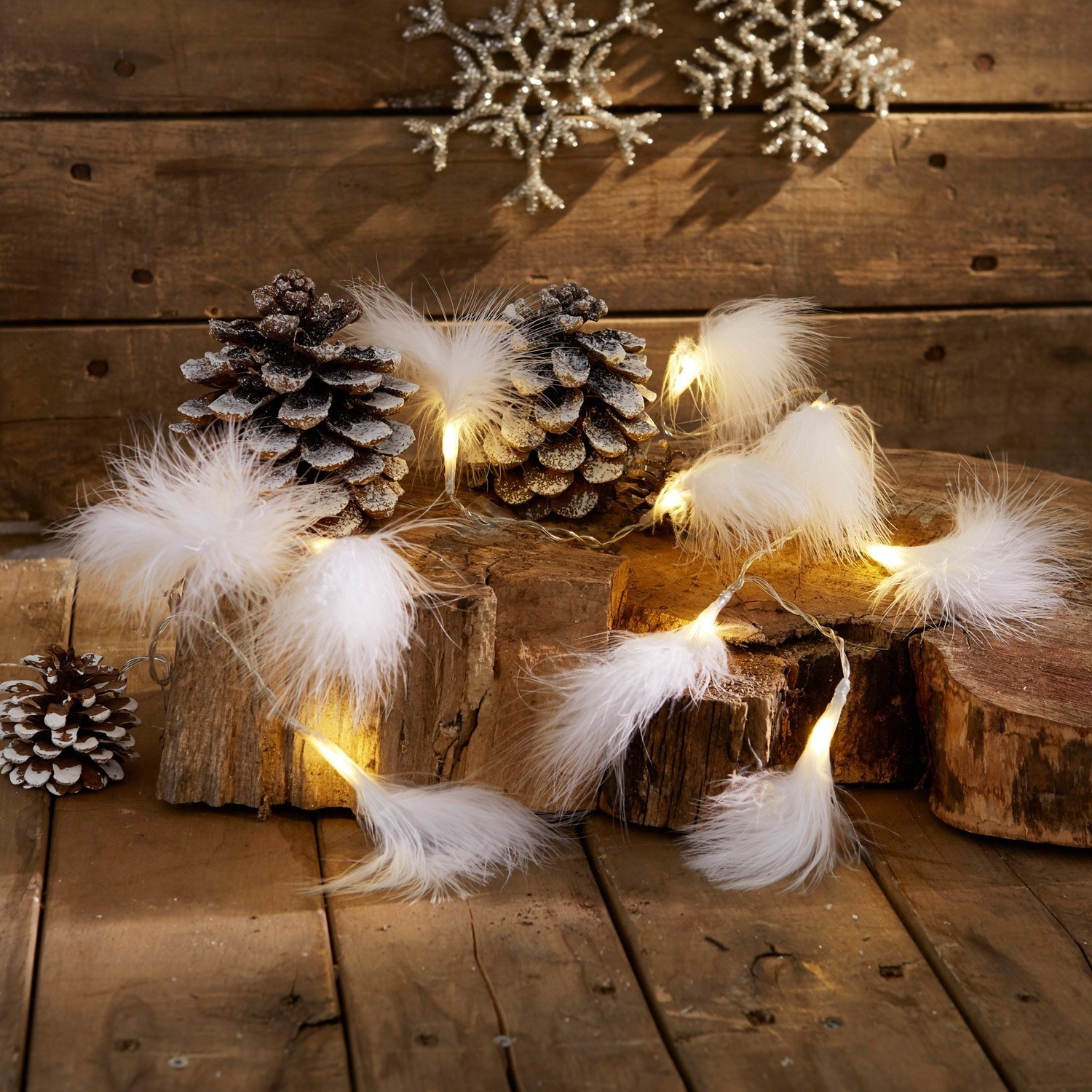 Catena luminosa con piume bianche su sfondo in legno con pigne e decorazioni invernali