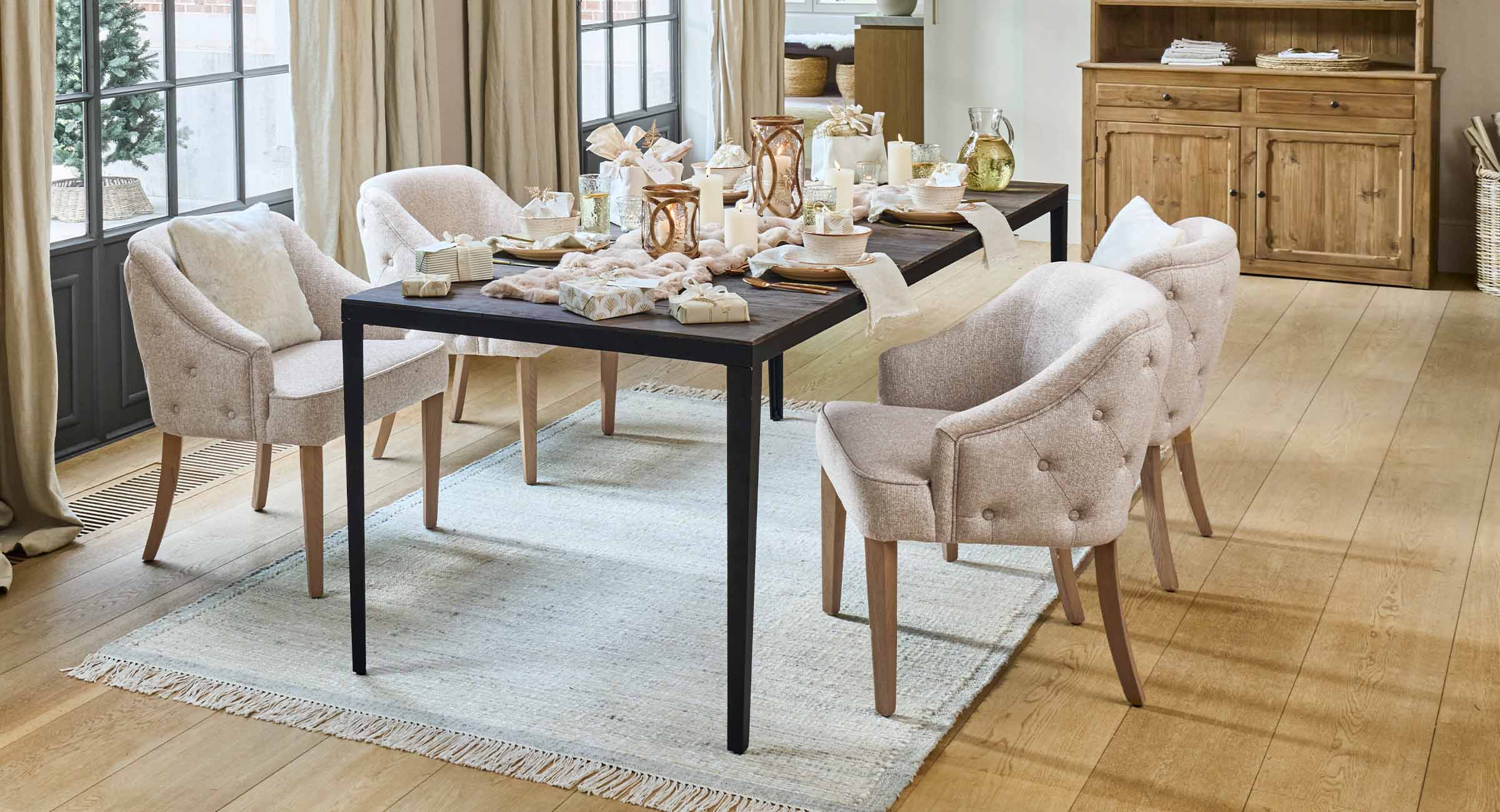 Sedie imbottite beige chiaro con gambe in legno attorno a tavolo scuro con candele e decorazioni in sala da pranzo