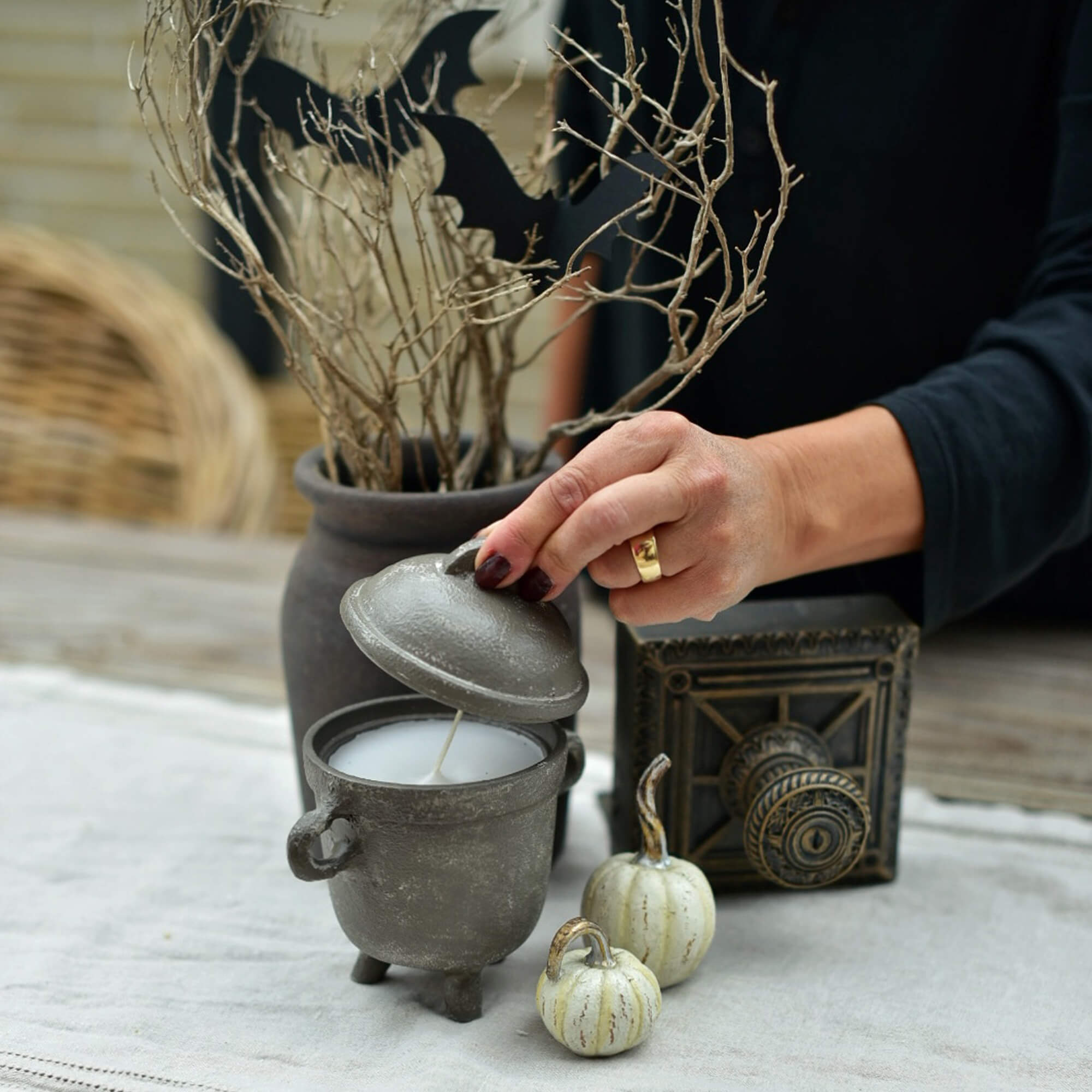 Candela grigia a forma di calderone con coperchio su tavolo decorato per Halloween con zucche e rami