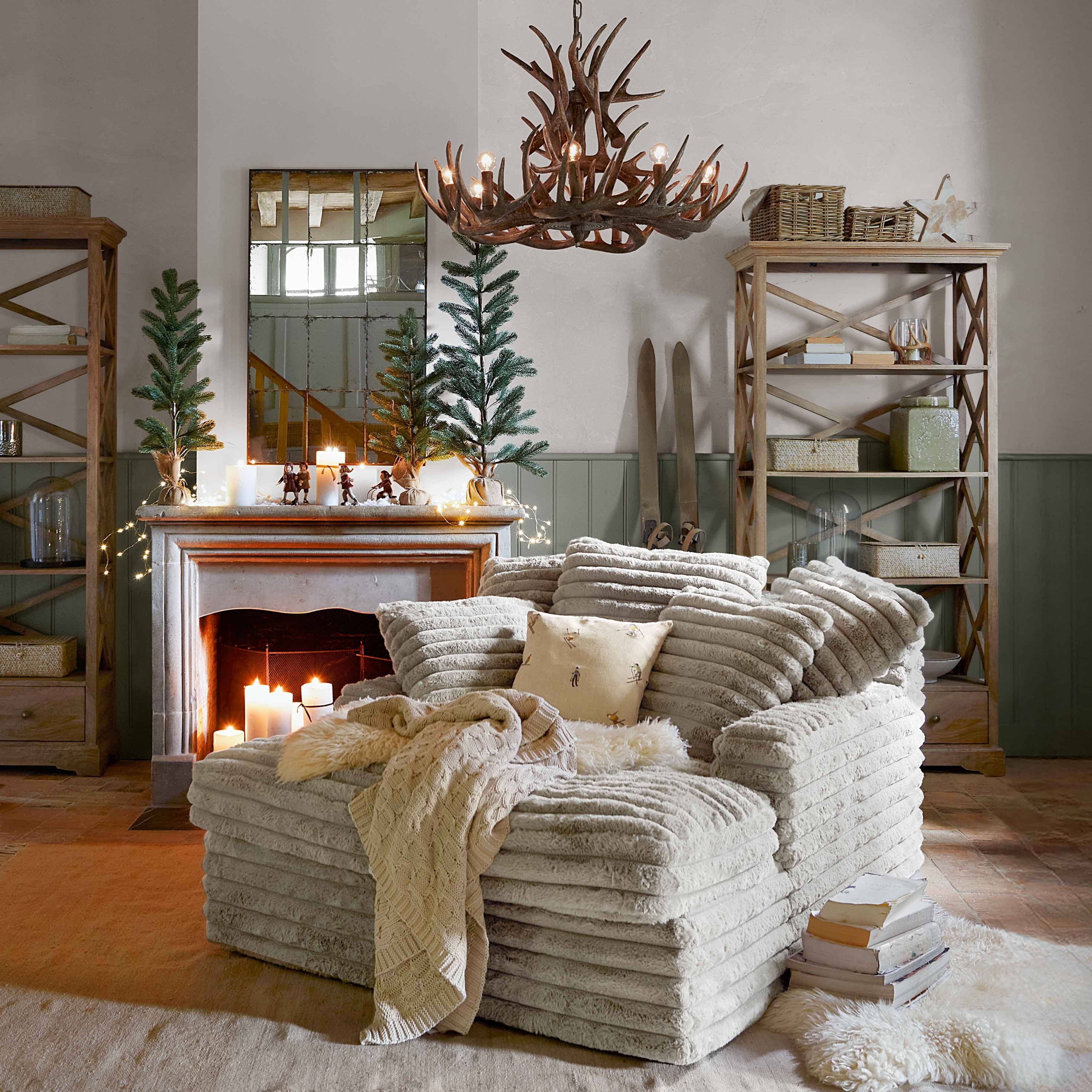 Poltrona beige in tessuto morbido con coperta e cuscino in soggiorno rustico con camino e decorazioni