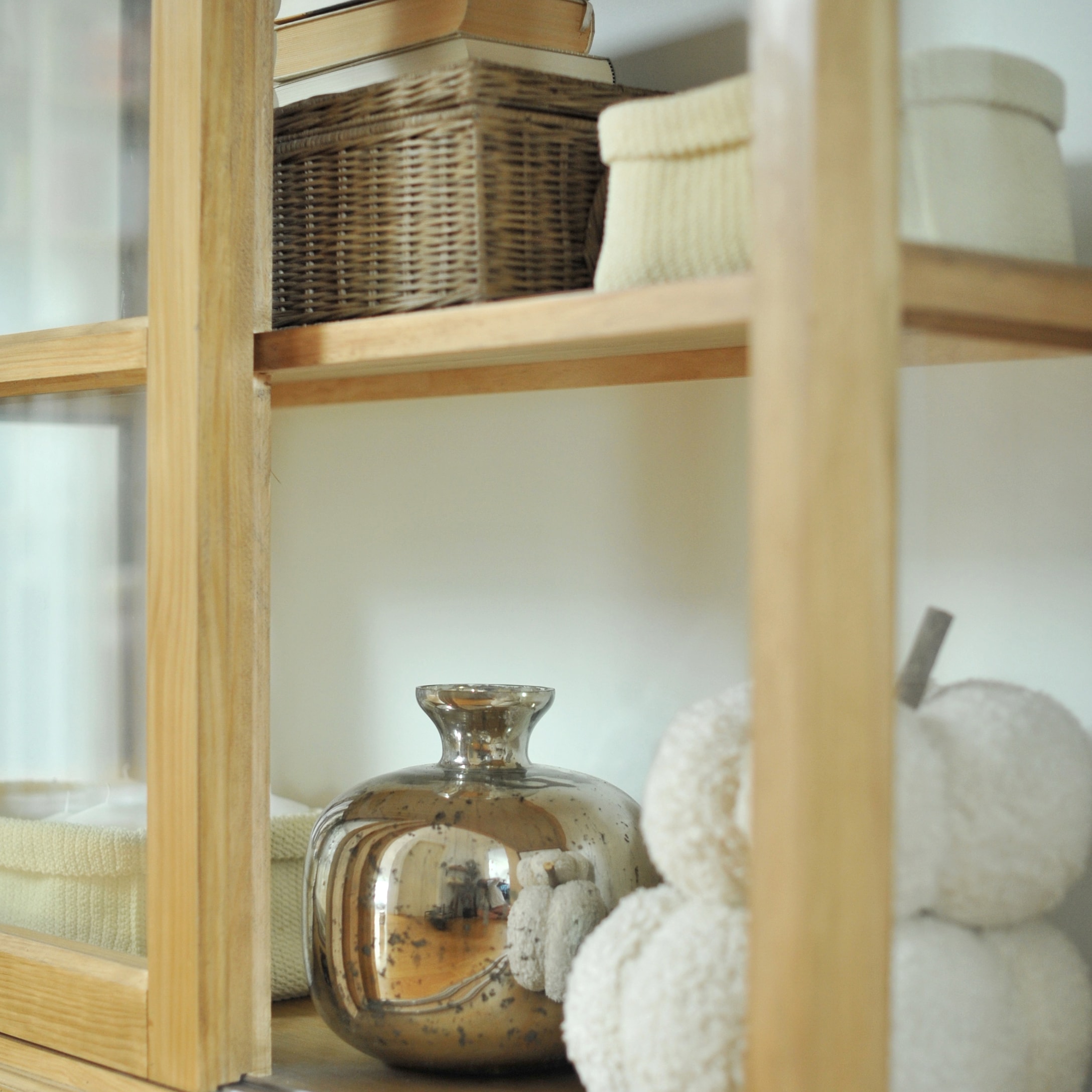 Vaso decorativo in vetro argentato su mensola in legno con cesto in vimini e morbidi cuscini crema